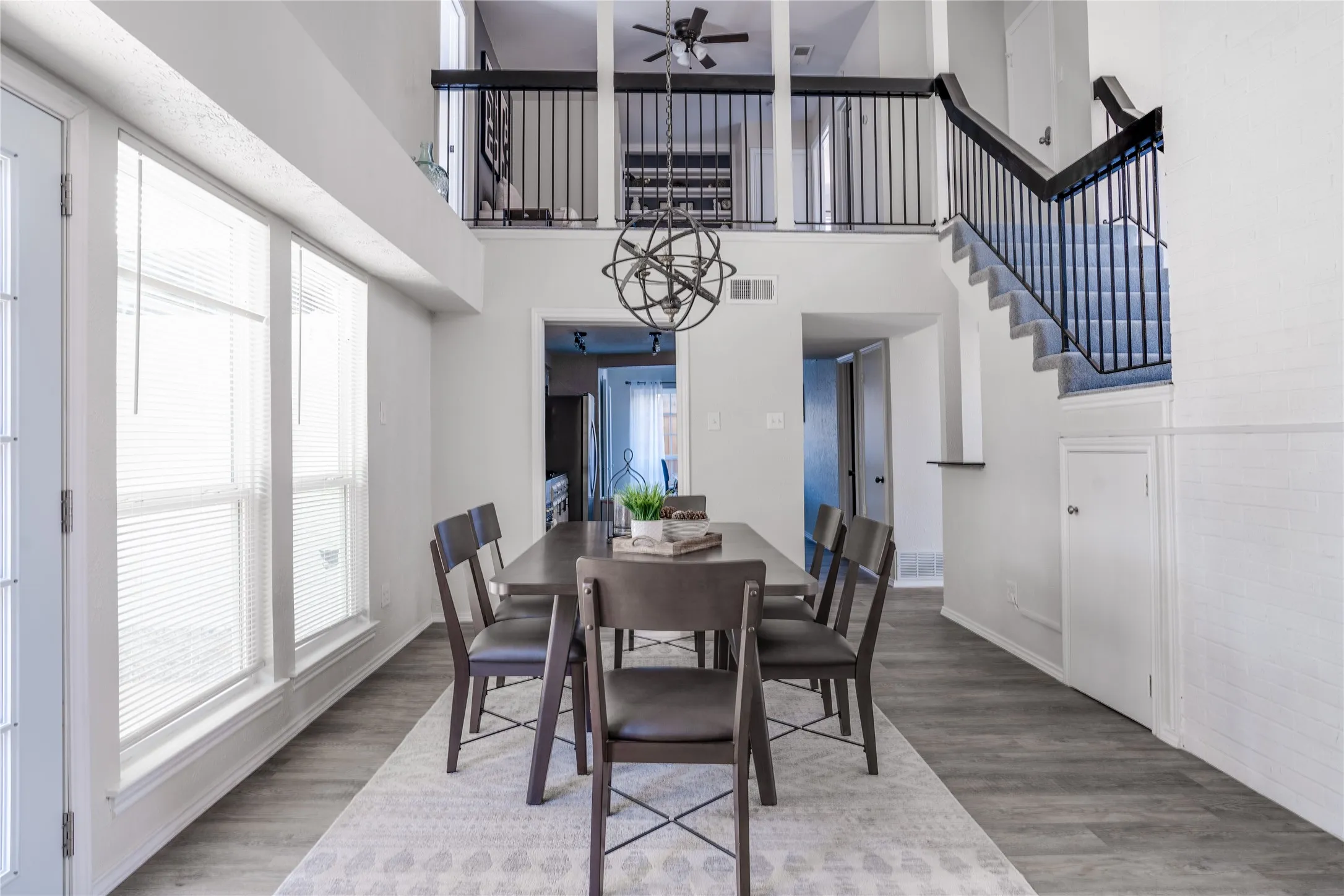 Vaulted ceiling, open concept design, wood-finish flooring, white paneled walls, and a black wrought iron staircase