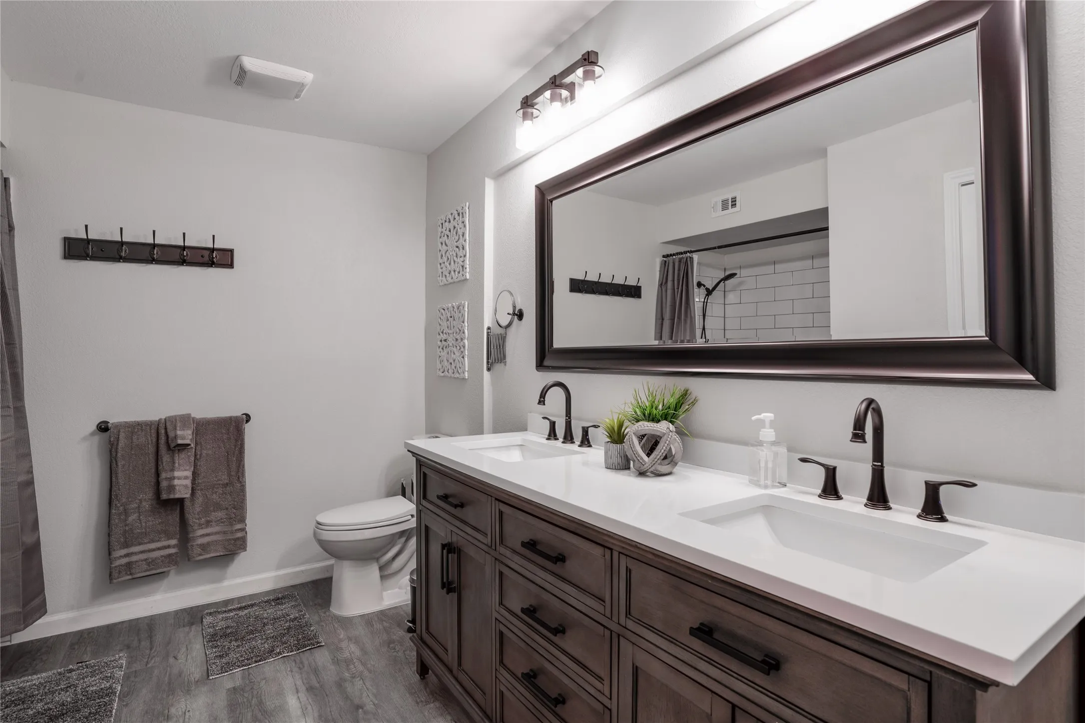 Dual sink vanity with dark wood-finish cabinetry, white countertops, and bronze-finish fixtures