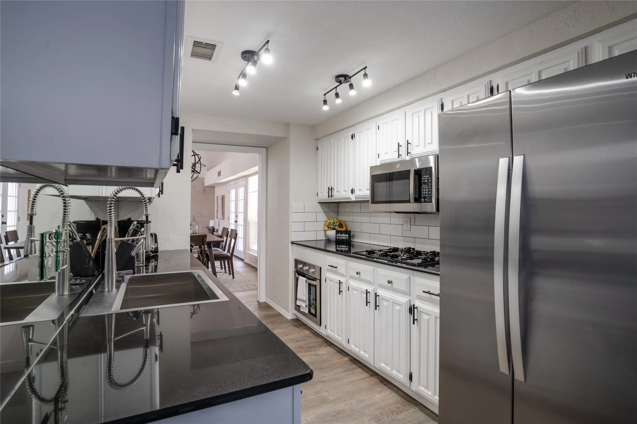 Kitchen featuring stainless steel appliances, white cabinetry, black countertops, a subway tile backsplash, and light wood-finish flooring