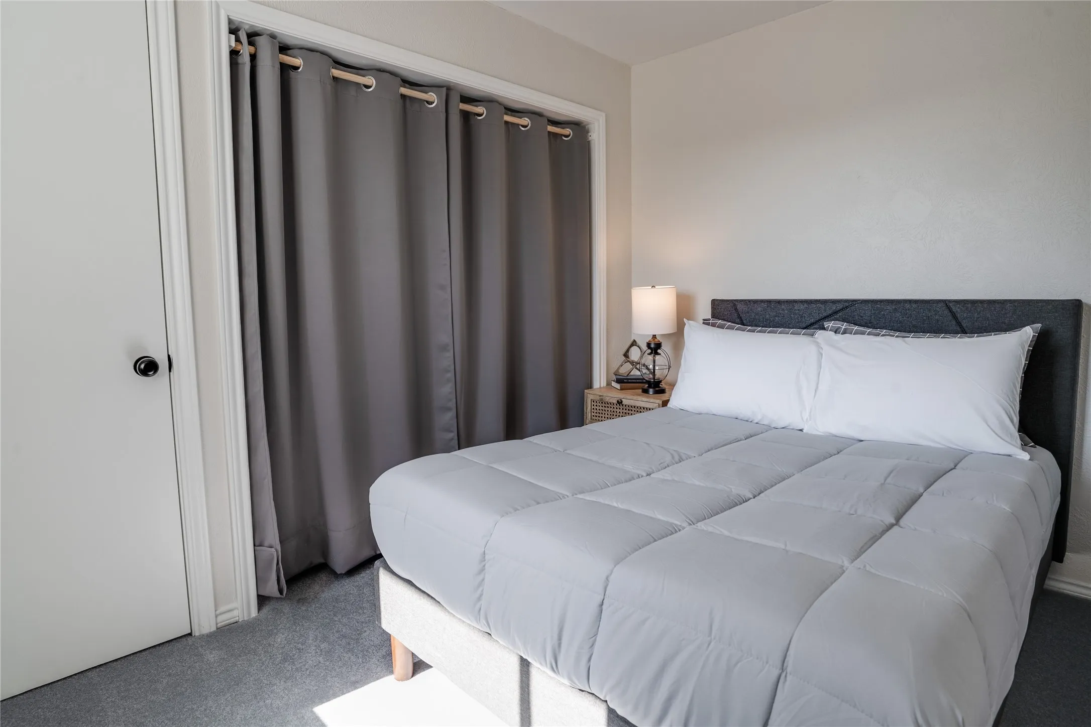 Carpeted flooring, white interior door with a black knob, and a gray fabric headboard