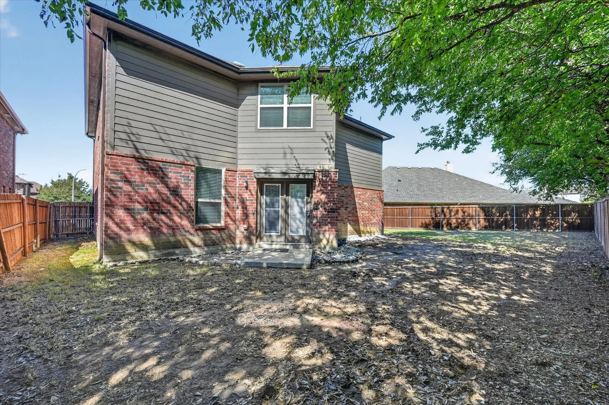 Spacious backyard with mature shade trees and expansive gravel hardscape