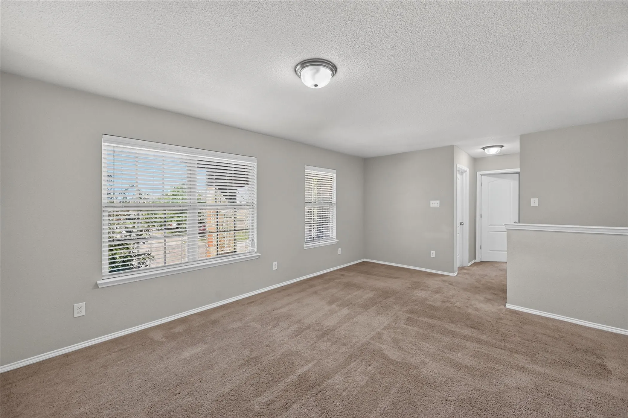 Carpeted room featuring multiple windows with blinds, a partial wall, and flush-mount lighting fixtures