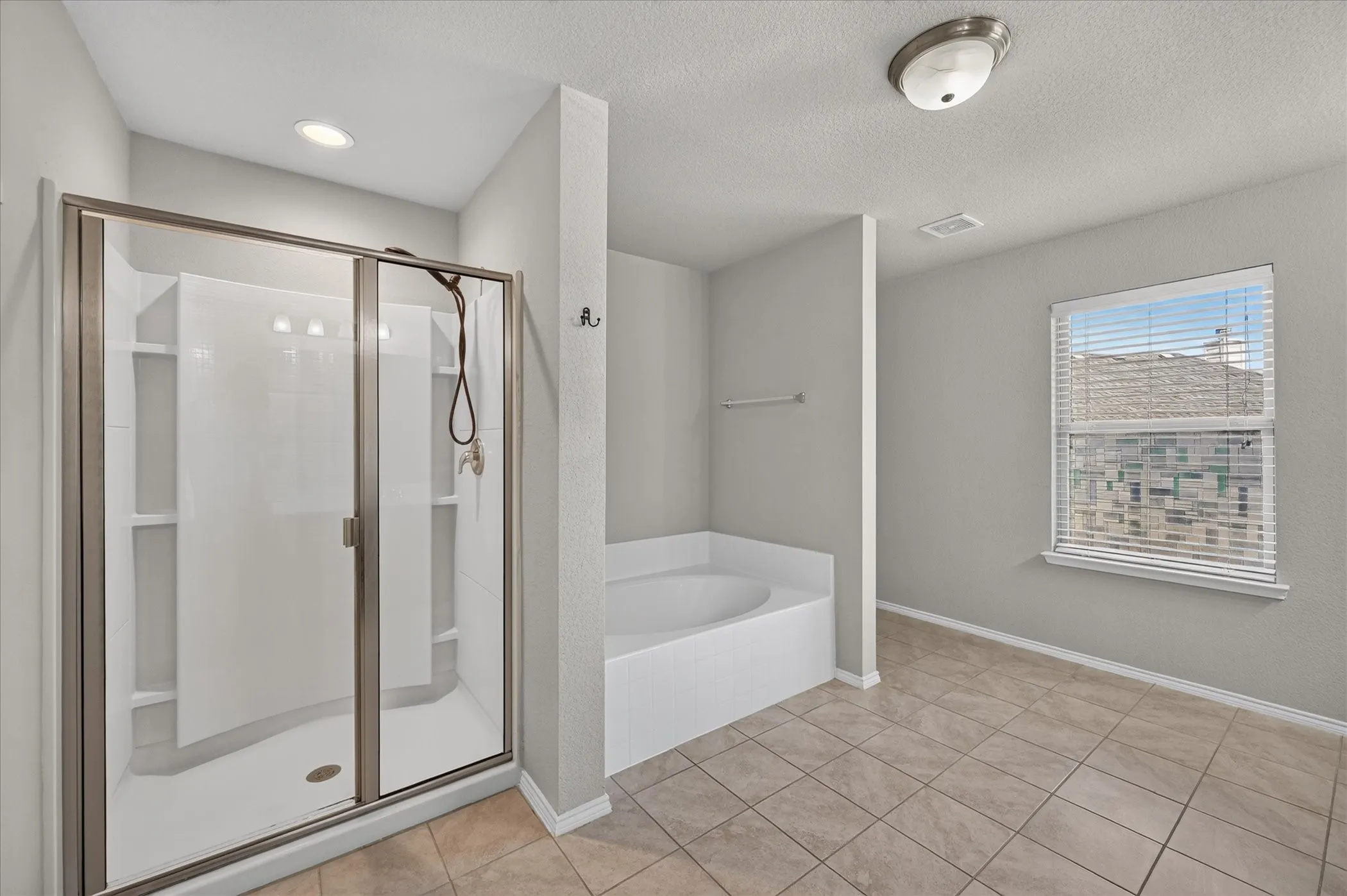 Spa-inspired primary bathroom featuring a frameless glass-enclosed shower with tile surround, freestanding soaking tub, tile flooring, recessed lighting, and a window with natural light