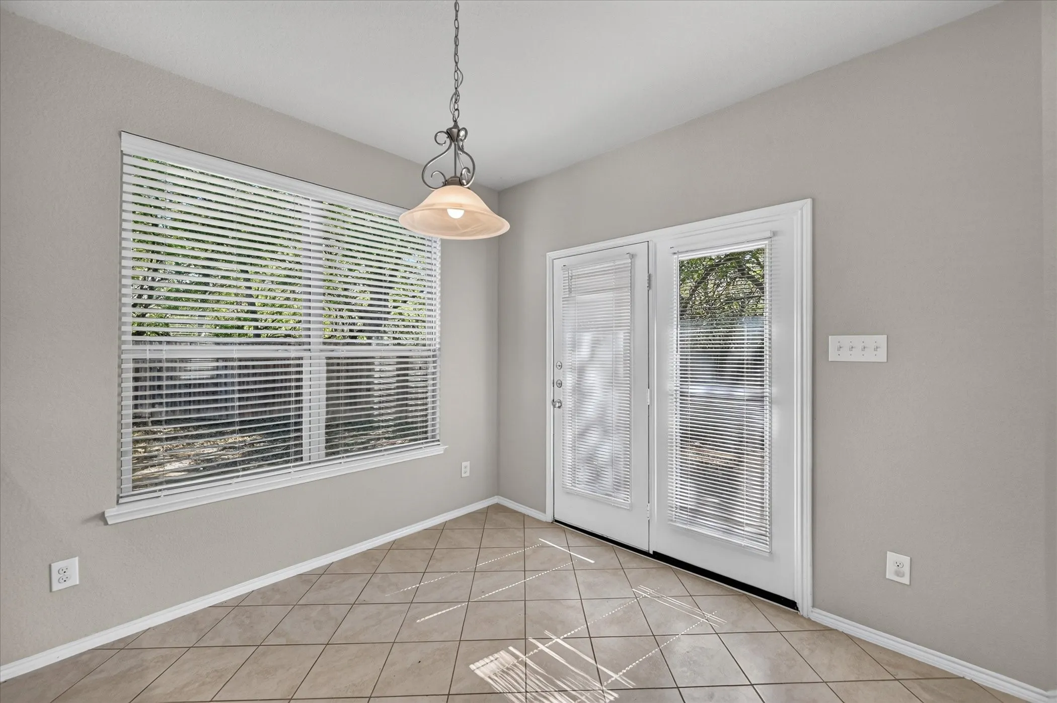 Bright sunroom showcasing diagonal tile flooring, large multi-pane windows with plantation shutters, French doors with integrated blinds, and a polished pendant light fixture overhead