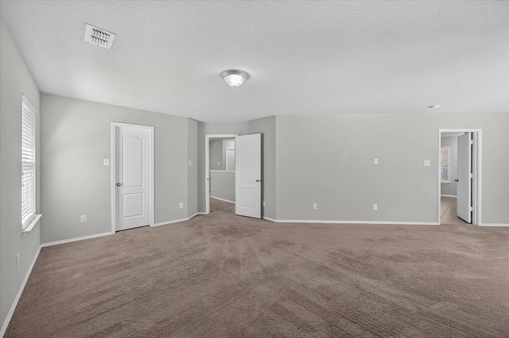 Spacious interior room with neutral-toned carpet, light gray wall finishes, multiple doorways, and a window with blinds