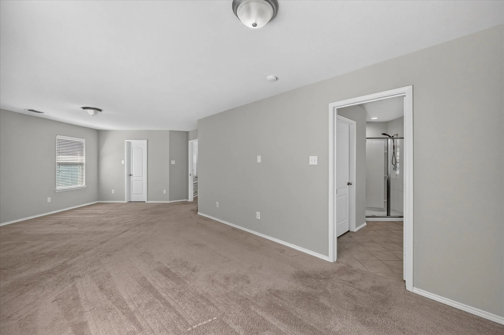 Spacious room with neutral gray walls, light brown carpet, and a window with blinds