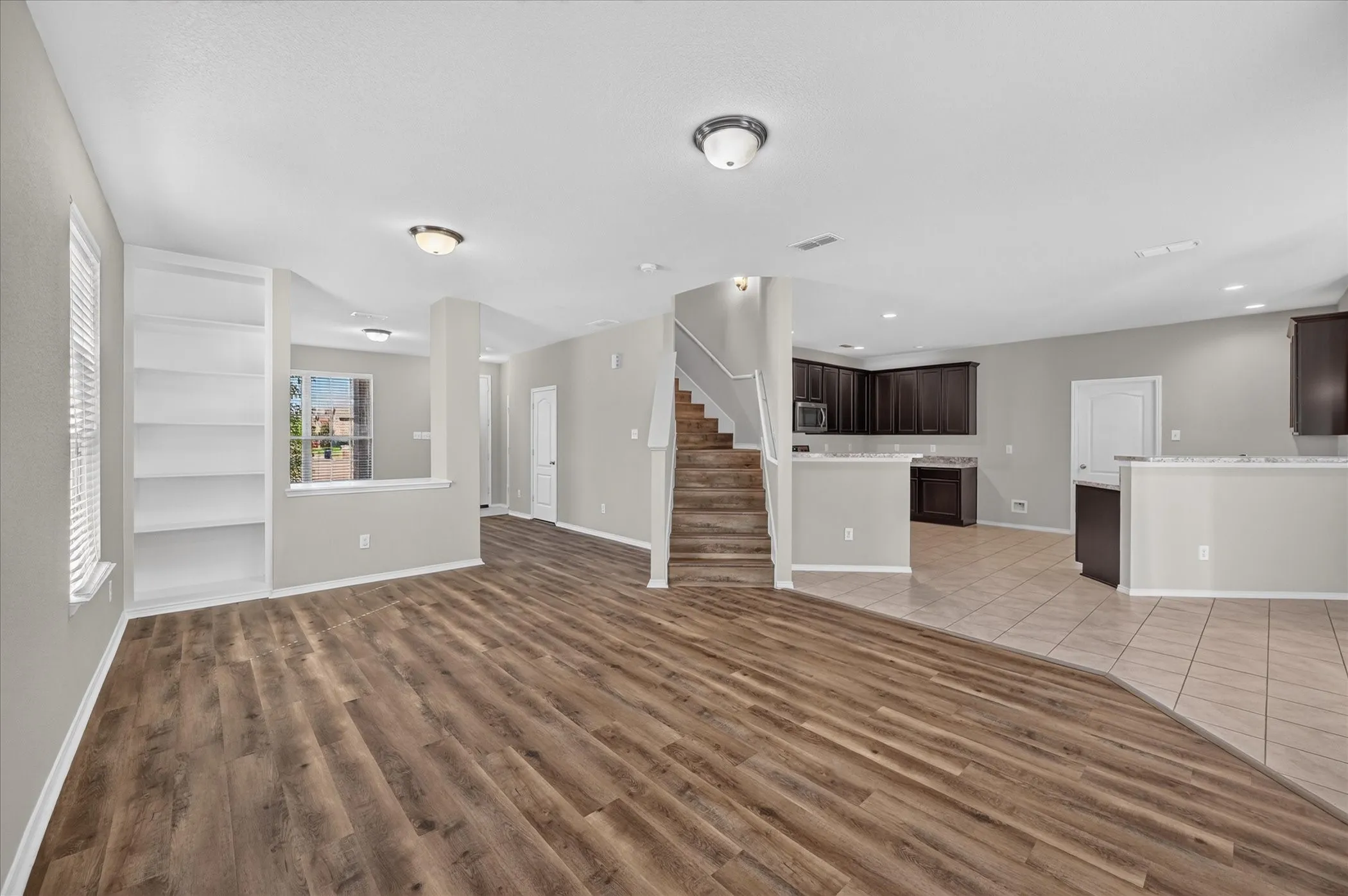 Expansive room featuring wood-finish flooring, built-in shelving, and a prominent staircase