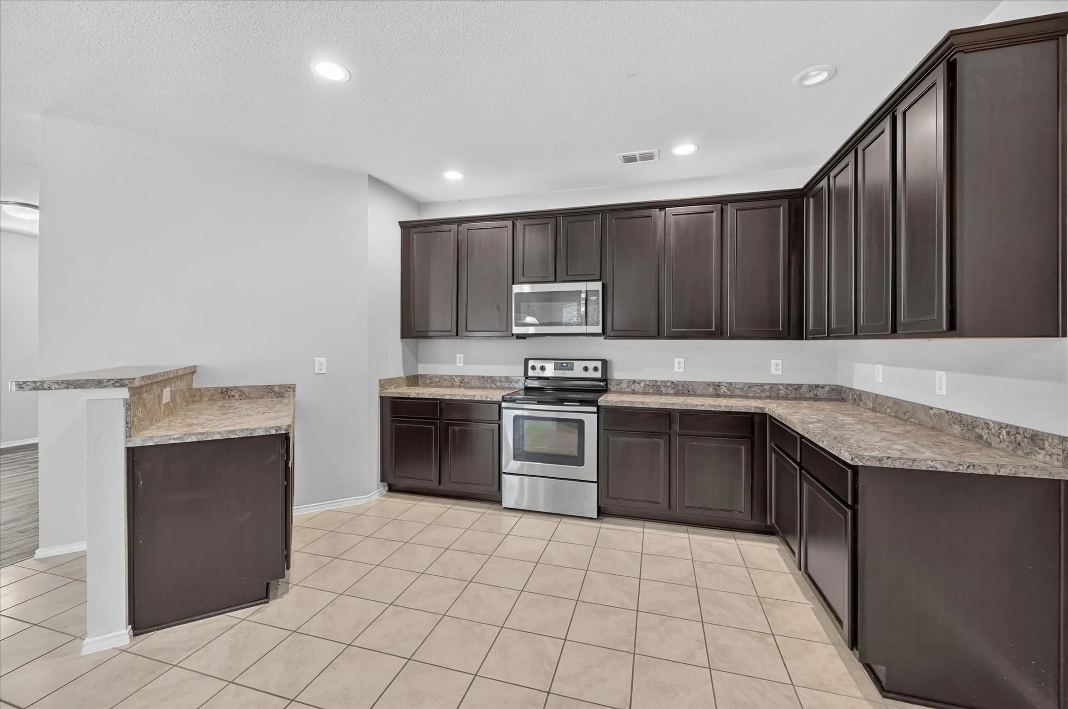 Kitchen featuring dark wood-finish cabinetry, light-toned countertops, stainless steel appliances, and tiled flooring
