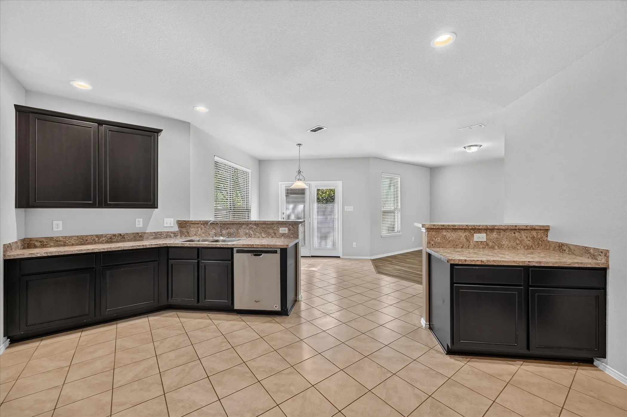Kitchen featuring dark cabinetry, light-toned countertops, a stainless steel dishwasher, and recessed lighting
