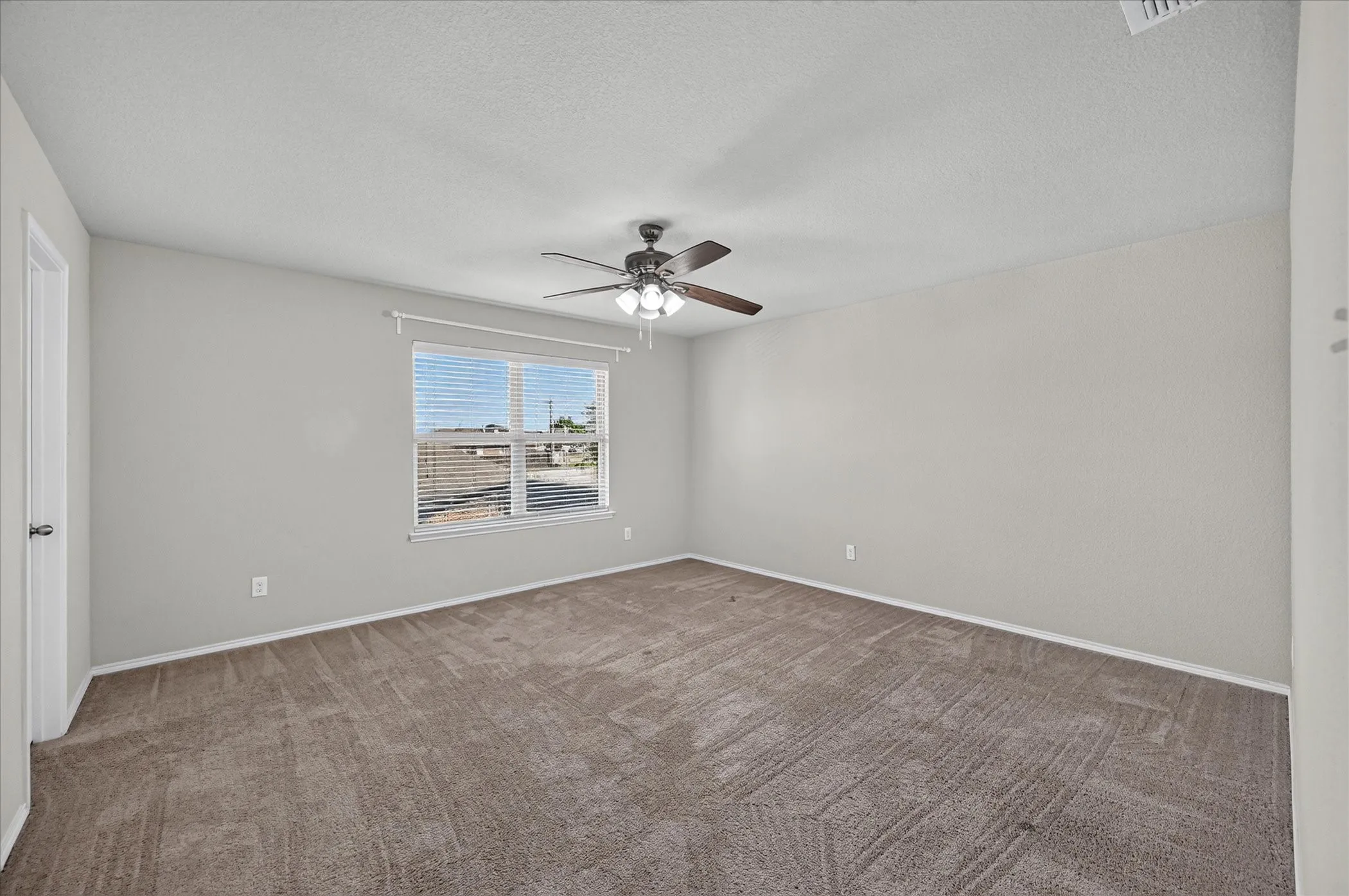 Carpeted room with a ceiling fan light fixture and a window featuring horizontal blinds
