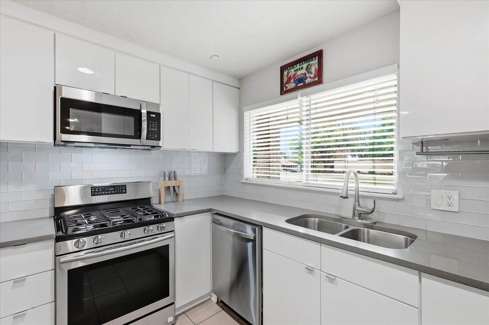 Kitchen featuring white cabinetry, gray quartz countertops, stainless steel appliances, a subway tile backsplash, and a double basin sink
