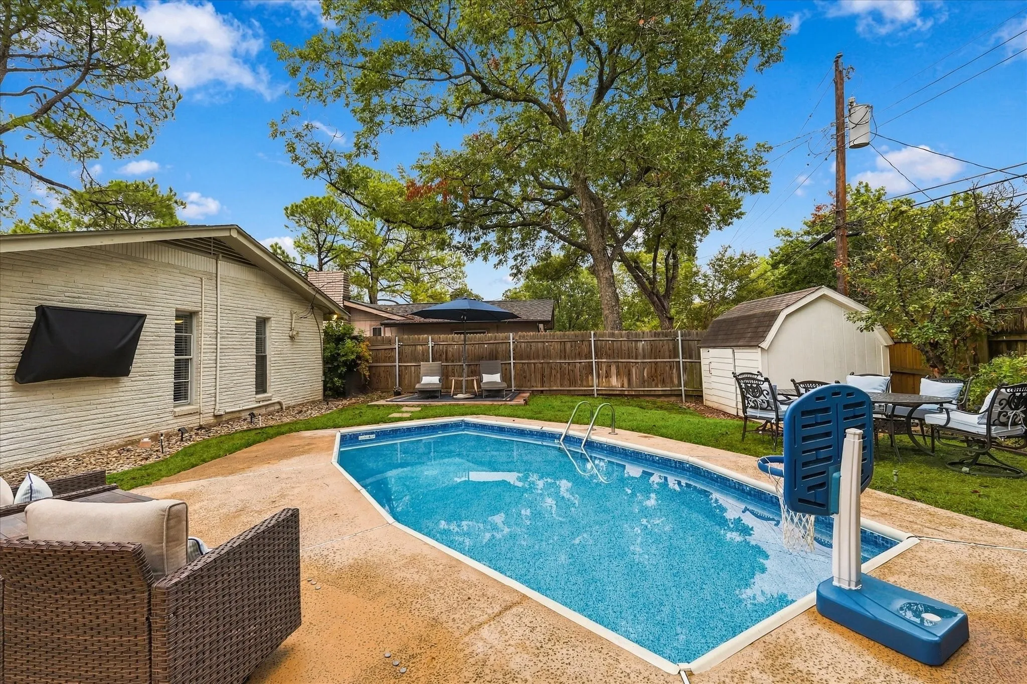 Expansive backyard featuring a swimming pool, a storage shed, a wood fence, and mature trees