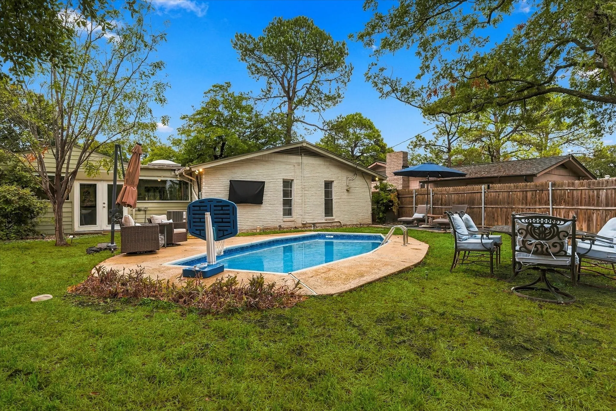 Expansive backyard featuring a built-in swimming pool with concrete coping, a wooden privacy fence, and mature trees
