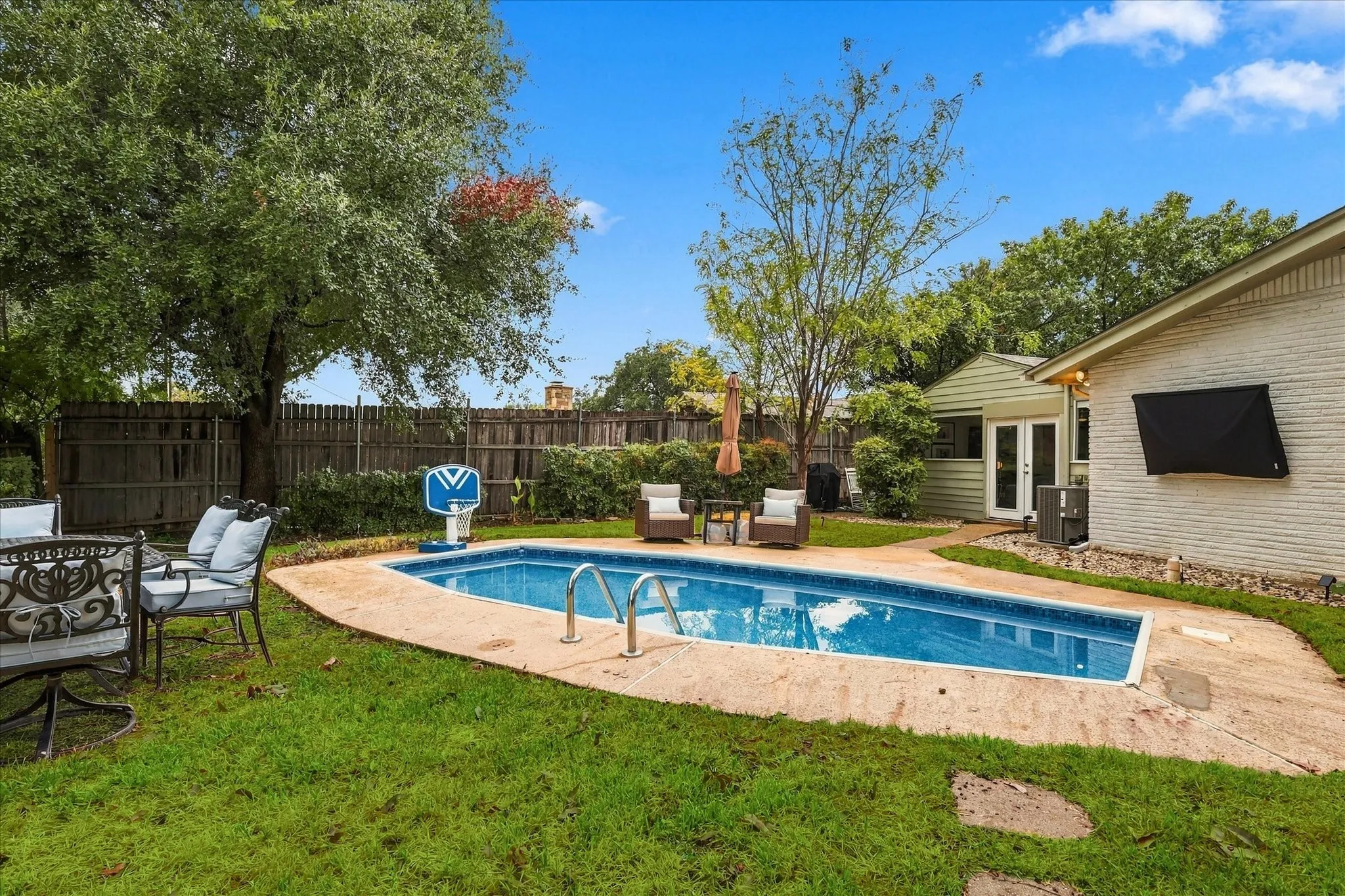 Rectangular swimming pool with concrete decking, surrounded by a manicured lawn and mature trees