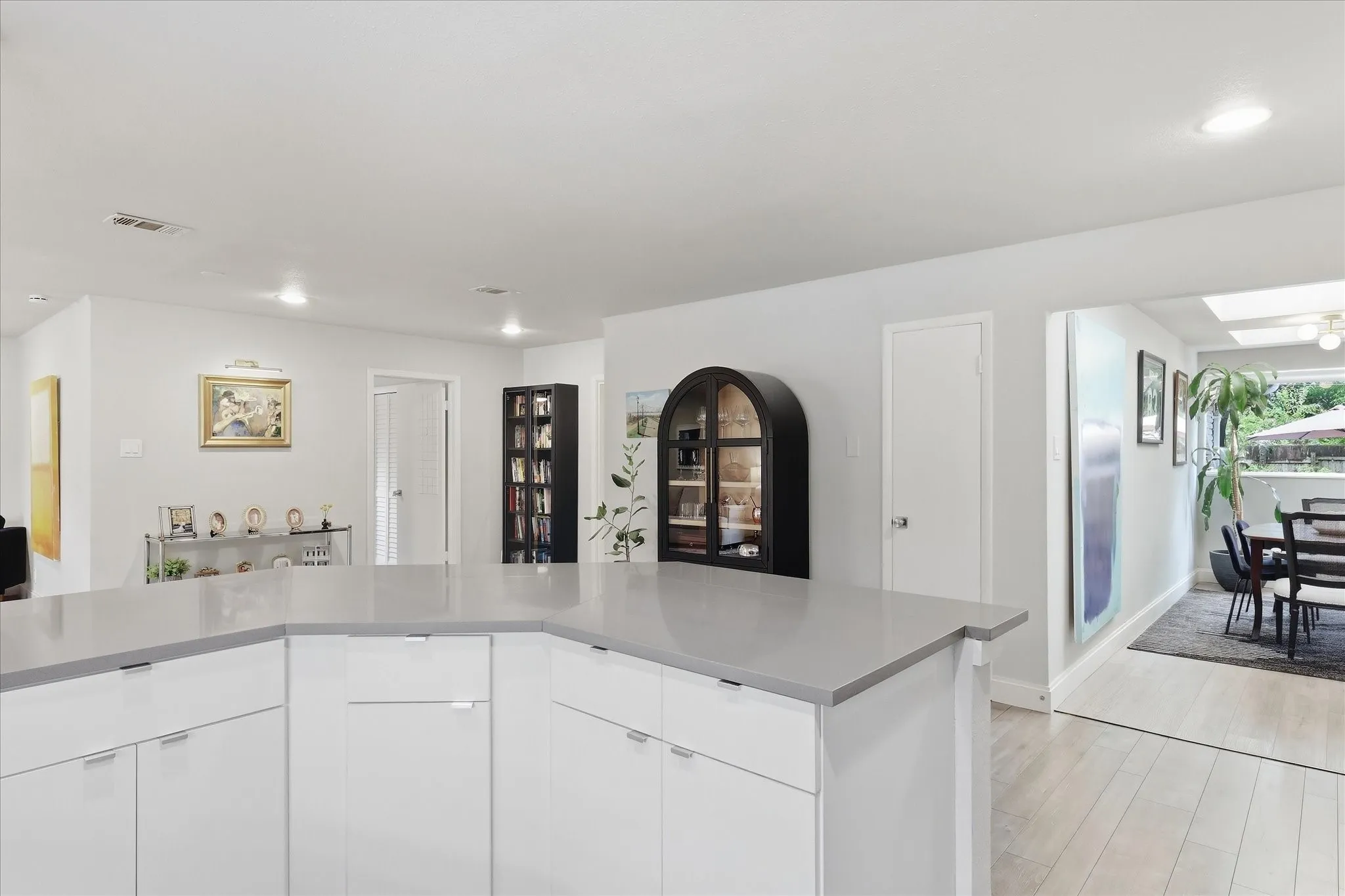 Modern kitchen featuring white cabinetry with stainless steel hardware, gray quartz countertops, and light wood-finish flooring