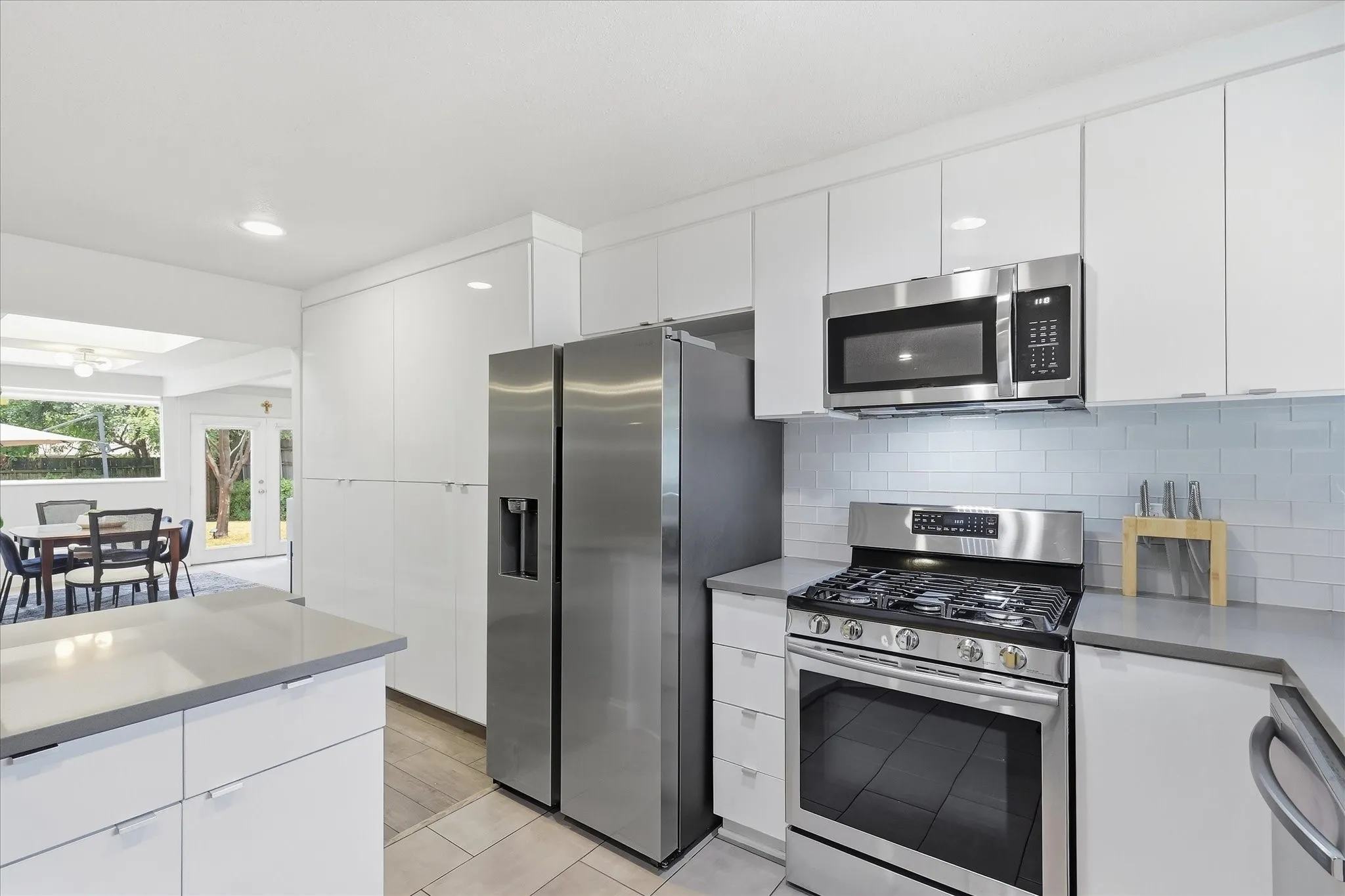Contemporary kitchen featuring white cabinetry, stainless steel appliances, gray quartz countertops, subway tile backsplash, and recessed lighting