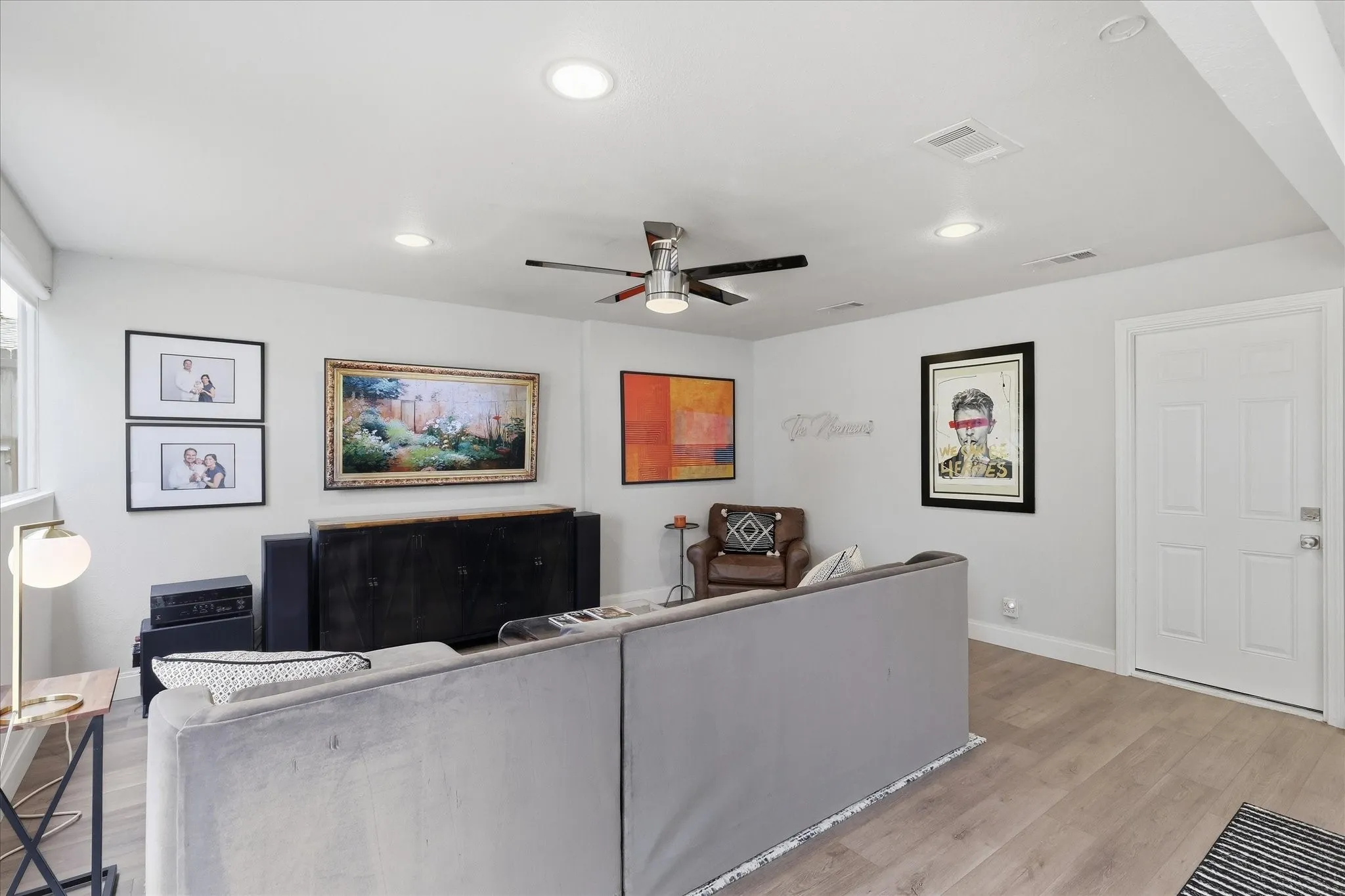 Recessed ceiling lighting, faux wood-finish flooring, ceiling fan, white paneled door, and a multi-pane window
