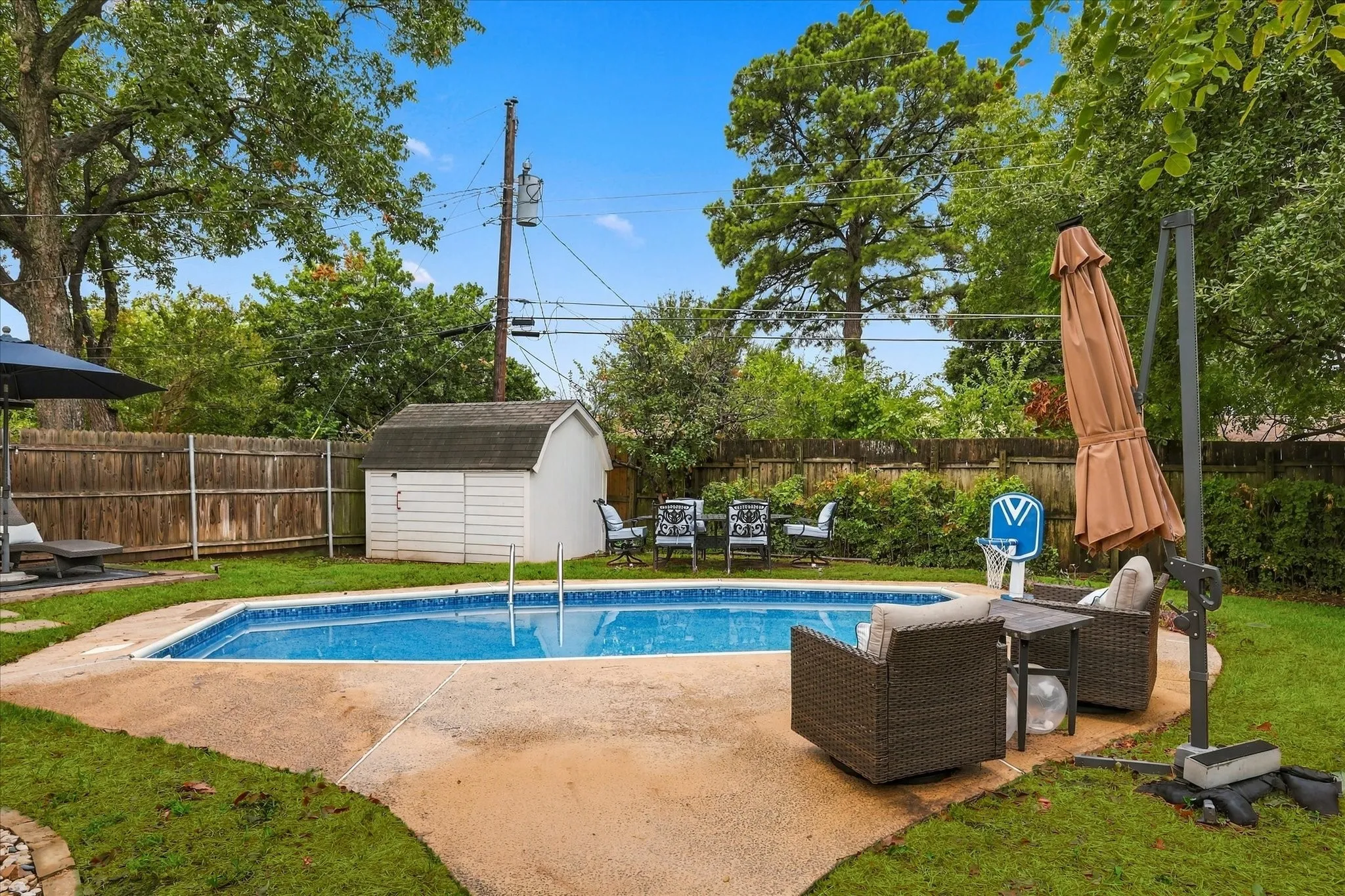 In-ground swimming pool with surrounding concrete patio, bordered by a wood privacy fence