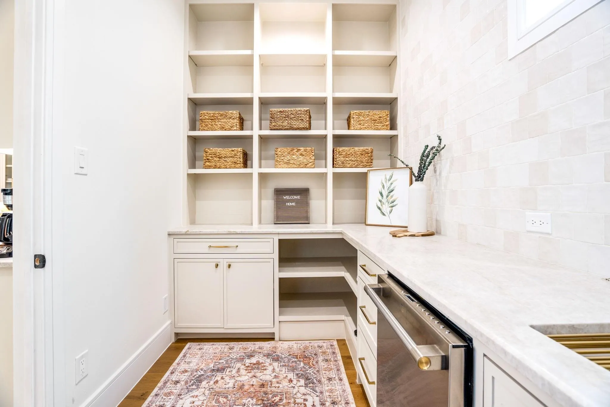 Built-in shelving, white cabinetry with gold-tone hardware, light-toned countertop, and a tiled backsplash