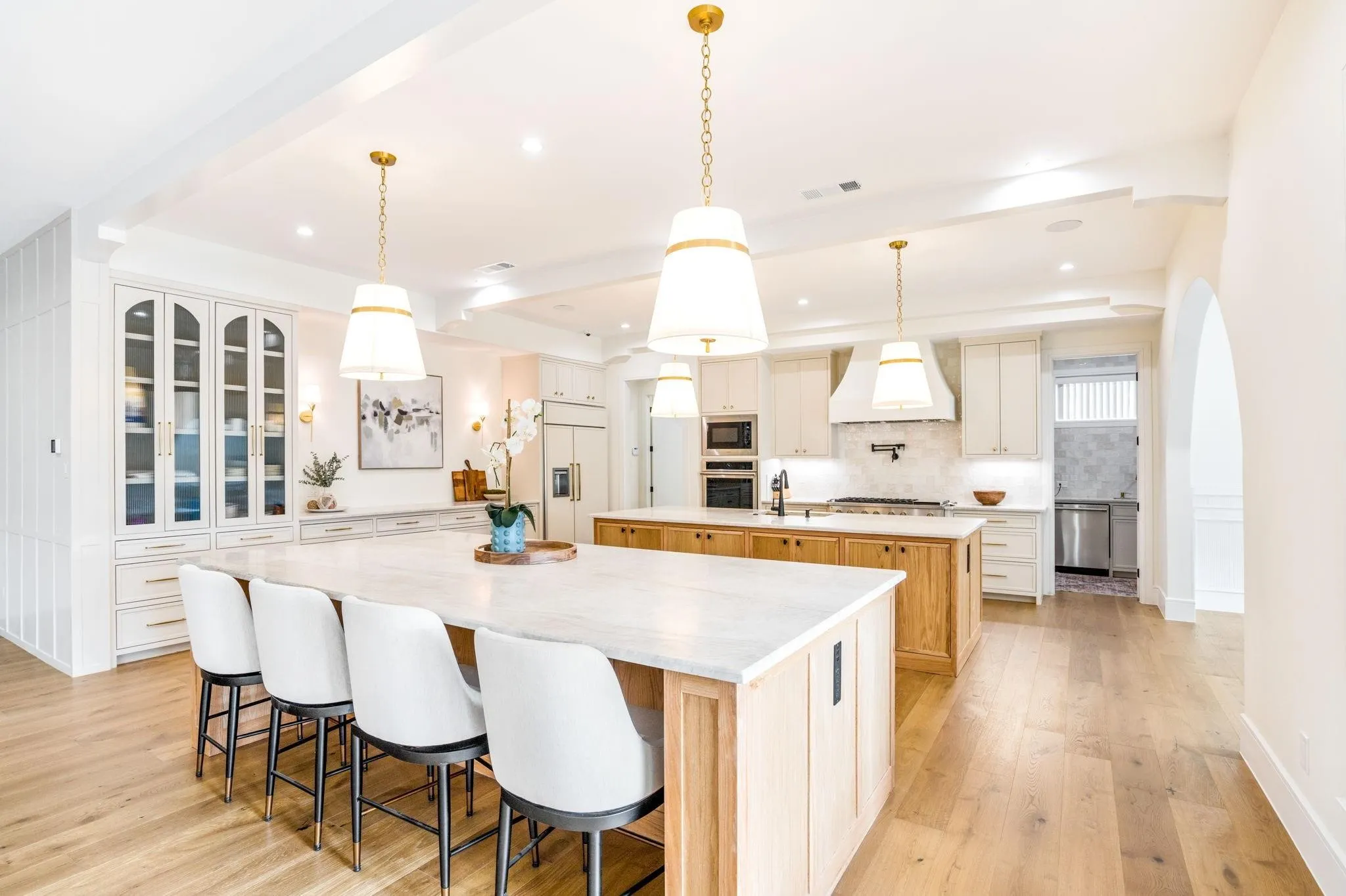 Gourmet kitchen featuring two islands with stone countertops, a built-in double oven, integrated refrigerator, and light wood-finish flooring
