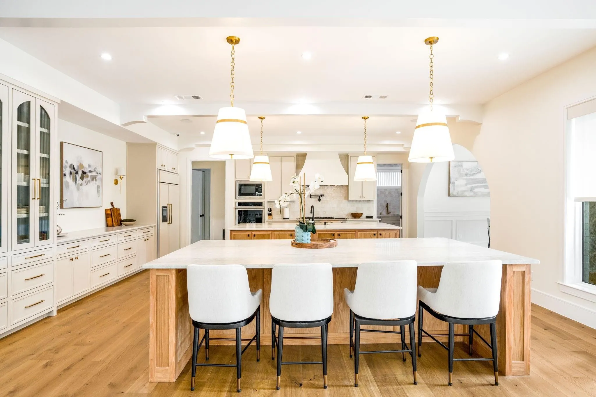 Wood-finish flooring, white cabinetry with gold-finish hardware, built-in double ovens, and a large kitchen island with seating