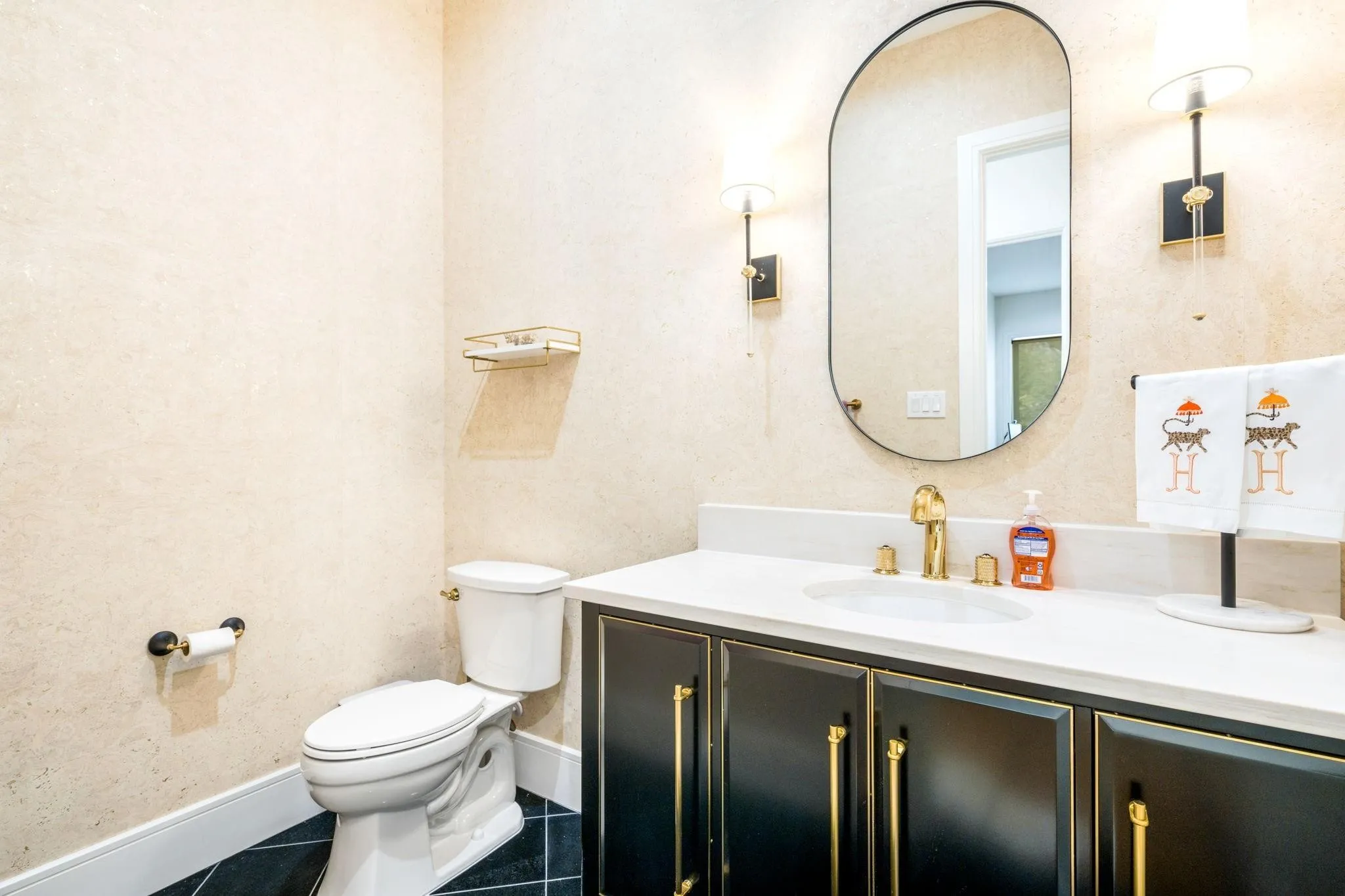 White countertop with an undermount sink, gold-finish faucet, and black vanity with gold-tone hardware