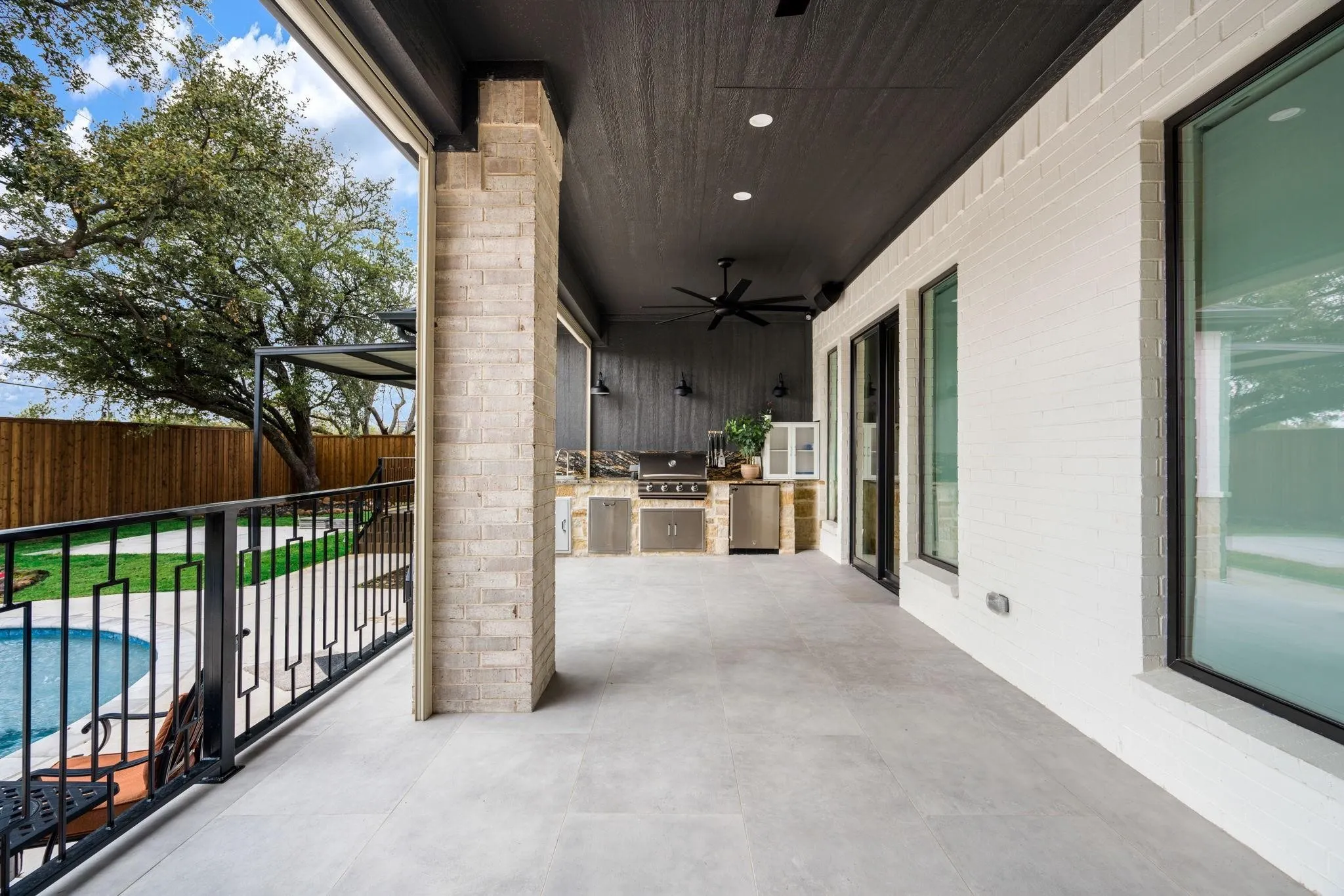 Expansive covered patio with recessed lighting, an outdoor kitchen featuring stainless steel appliances, a ceiling fan, and a light brick support column