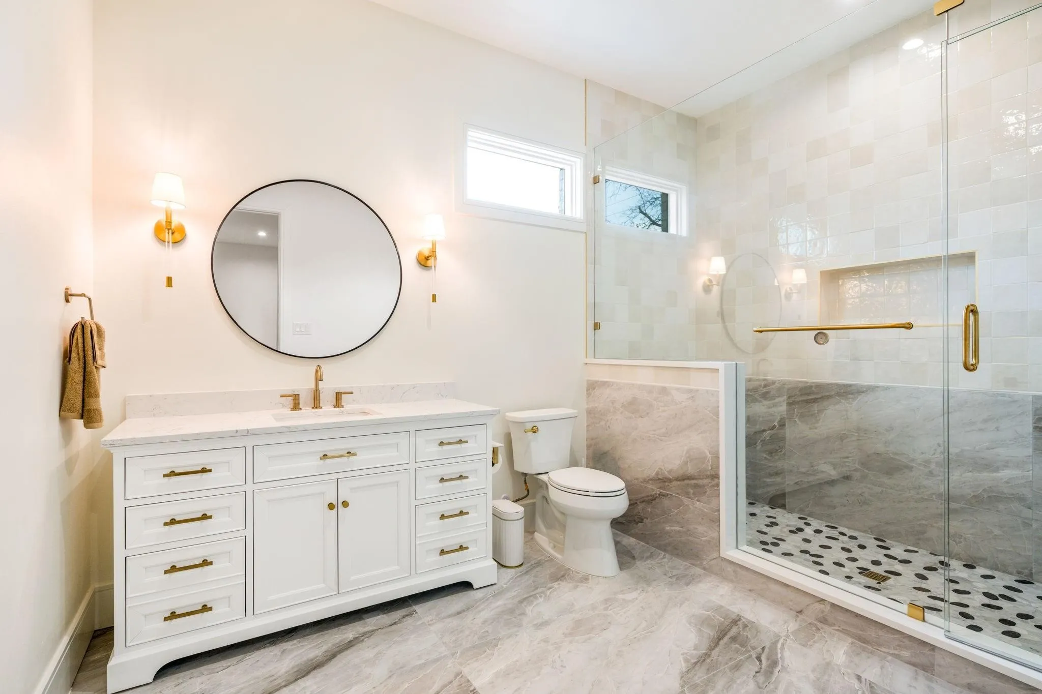 White vanity with gold-finish hardware and faucet, circular mirror, and two wall sconces