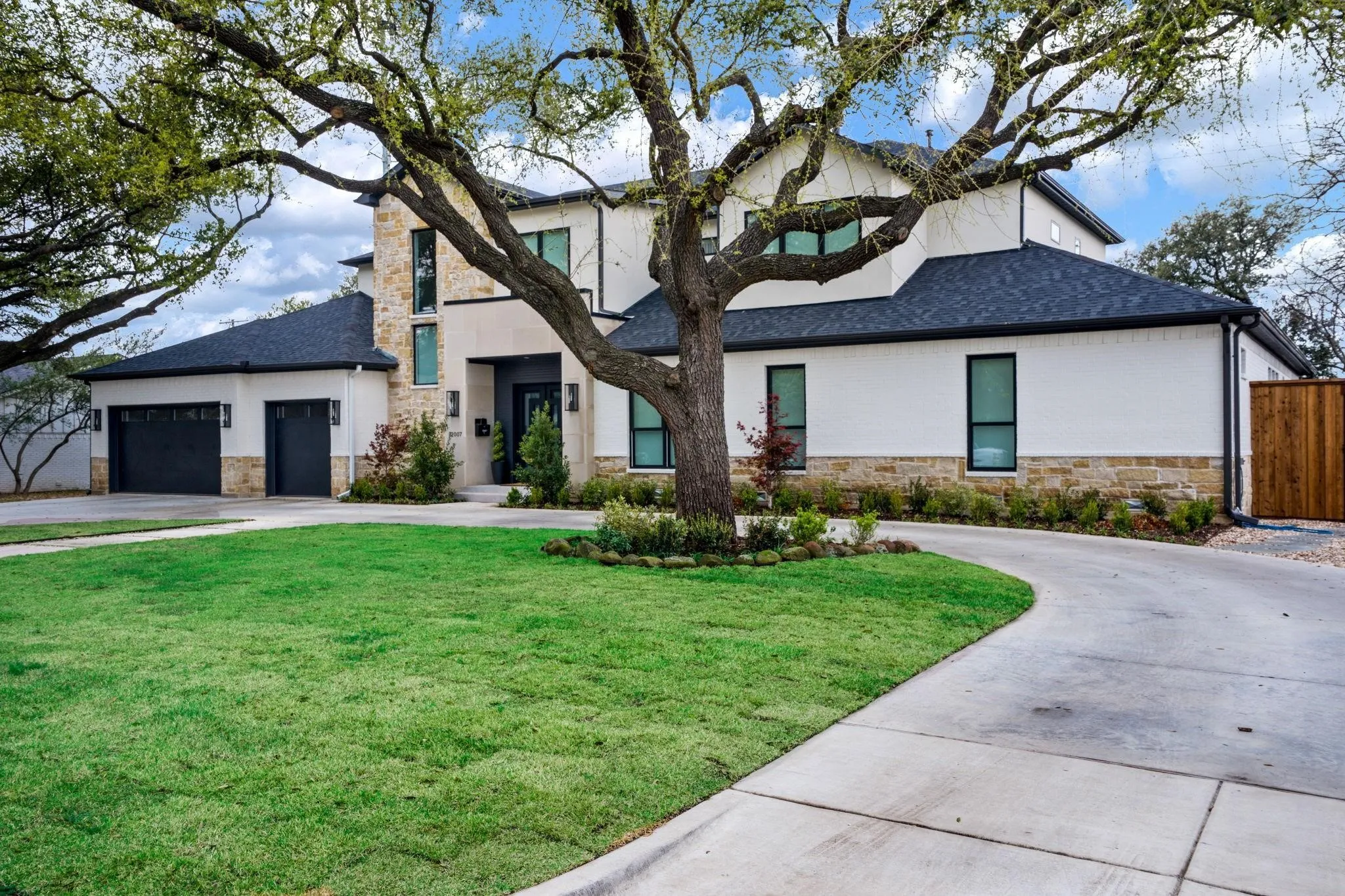 Modern exterior featuring a prominent stone facade, white stucco, dark-framed windows, a black shingle roof, and a concrete driveway