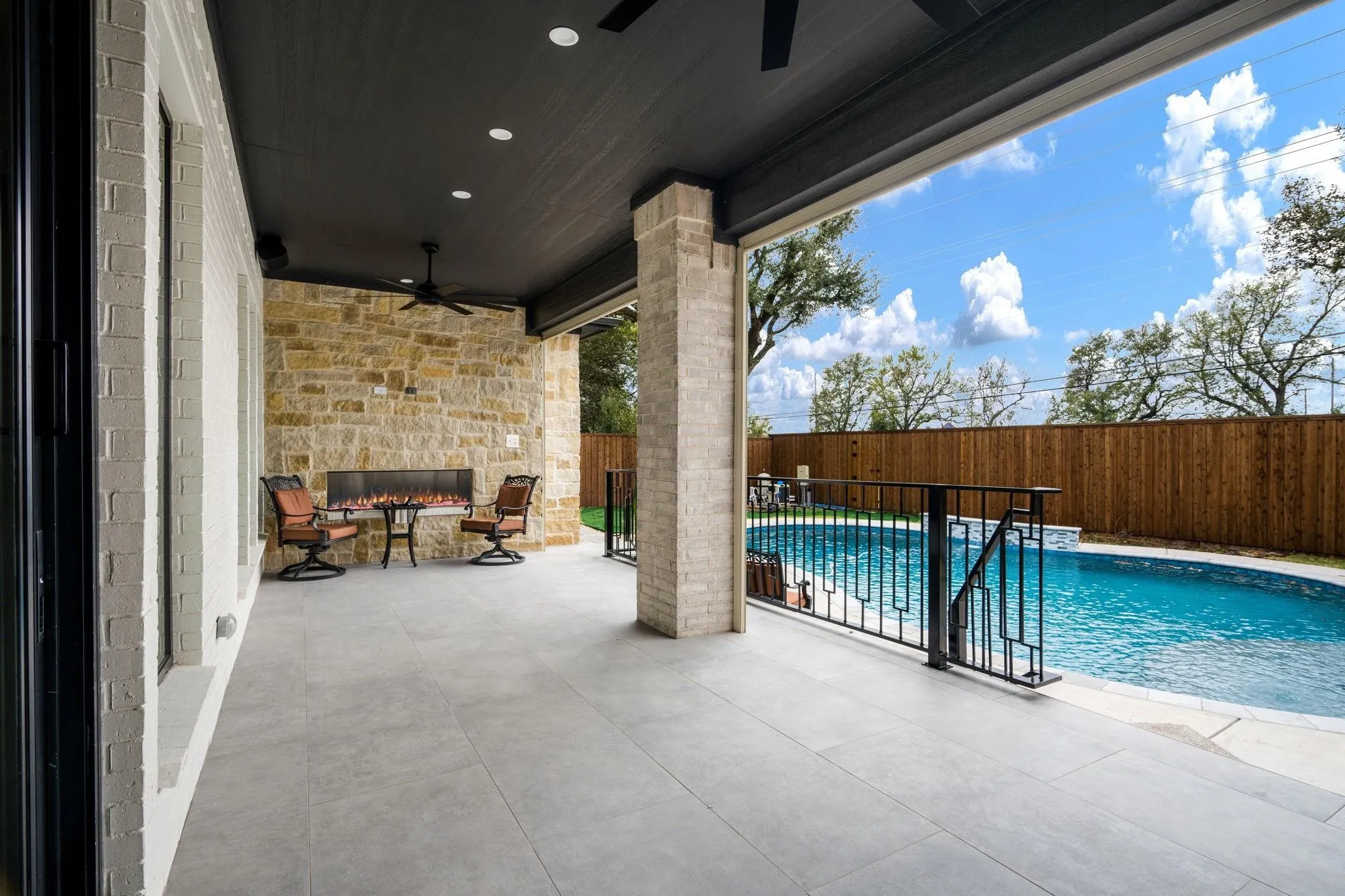 Covered patio with recessed lighting, ceiling fan, stone-clad wall, linear fireplace, and direct access to a swimming pool