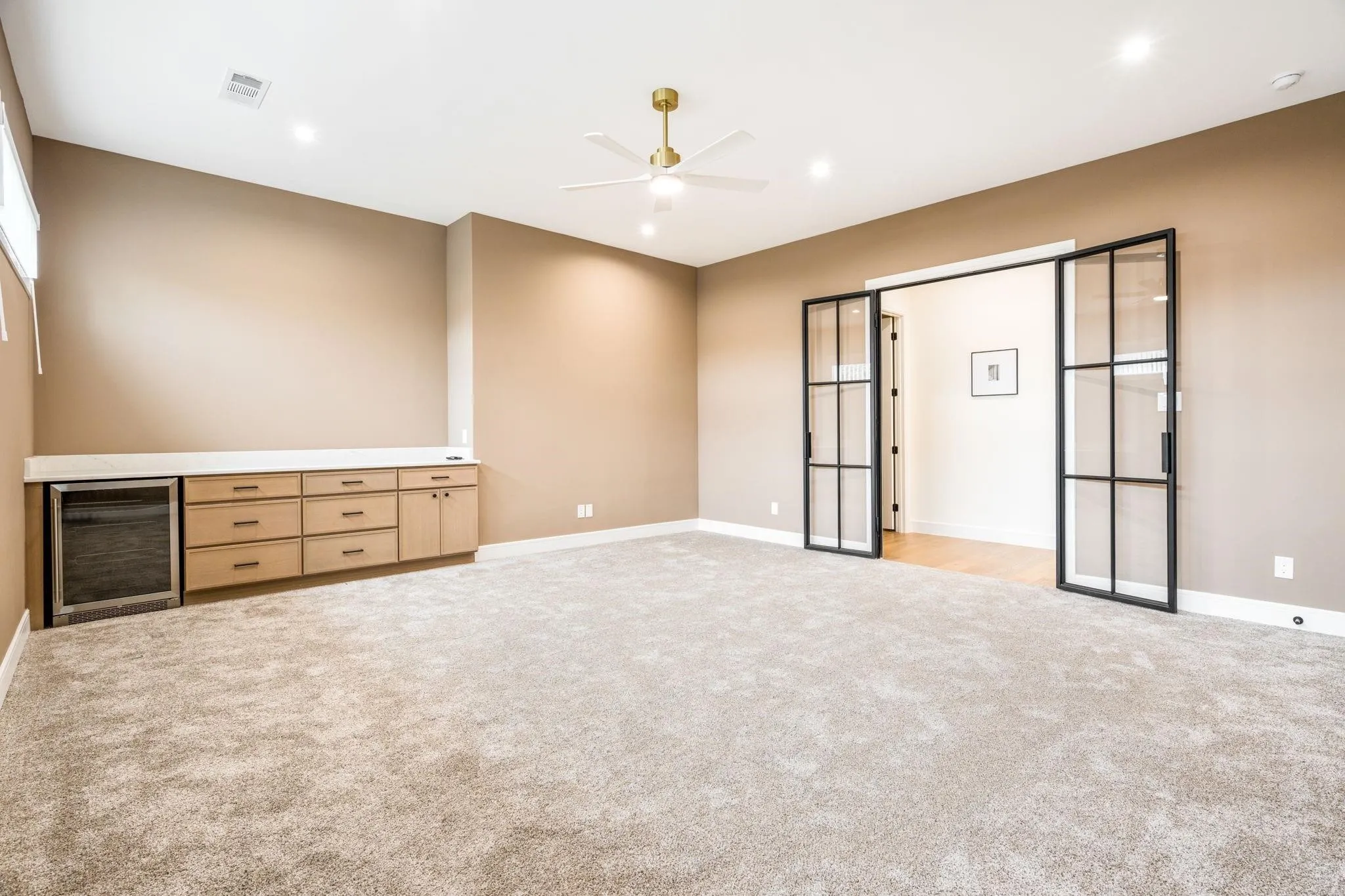 Built-in cabinetry with integrated beverage cooler, light-colored carpeting, recessed lighting, ceiling fan, and black-framed glass panel doors