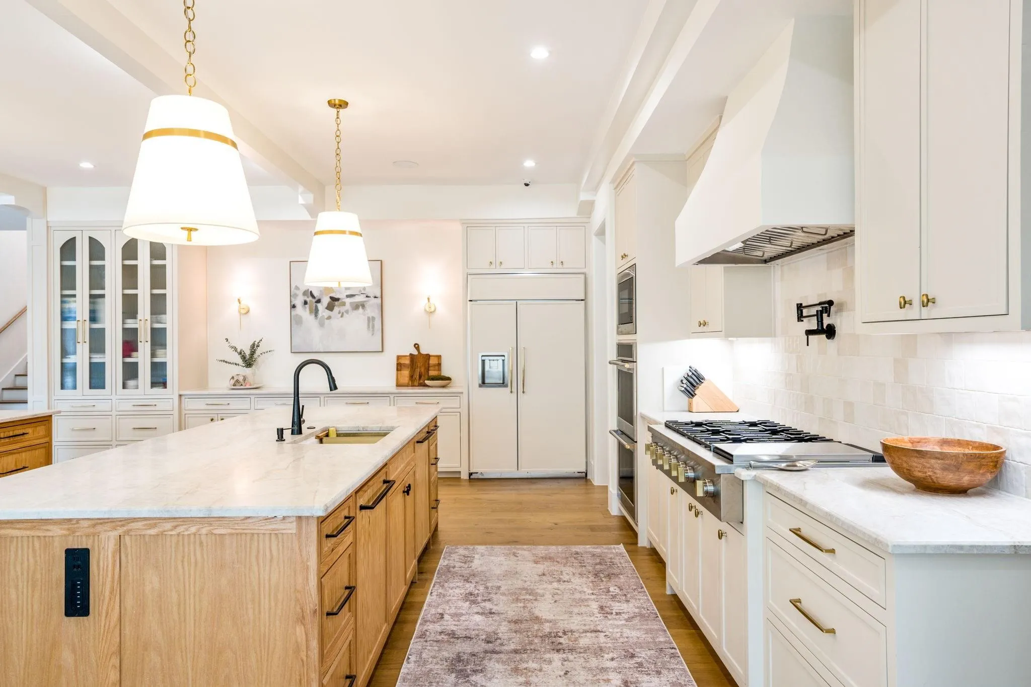 Gourmet kitchen featuring a large central island with a sink, built-in range, double wall ovens, and custom cabinetry