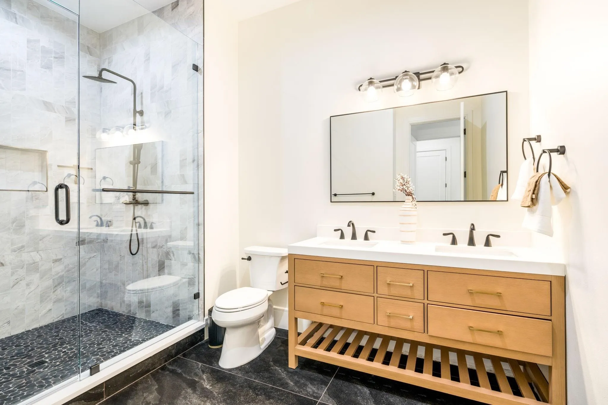 Glass-enclosed shower with stone tile surround and pebbled floor