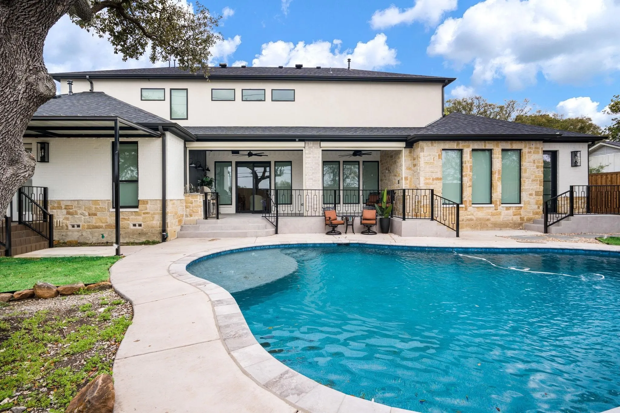 Outdoor swimming pool with a curved border, stone and stucco exterior, covered patio, and multi-level landscaping