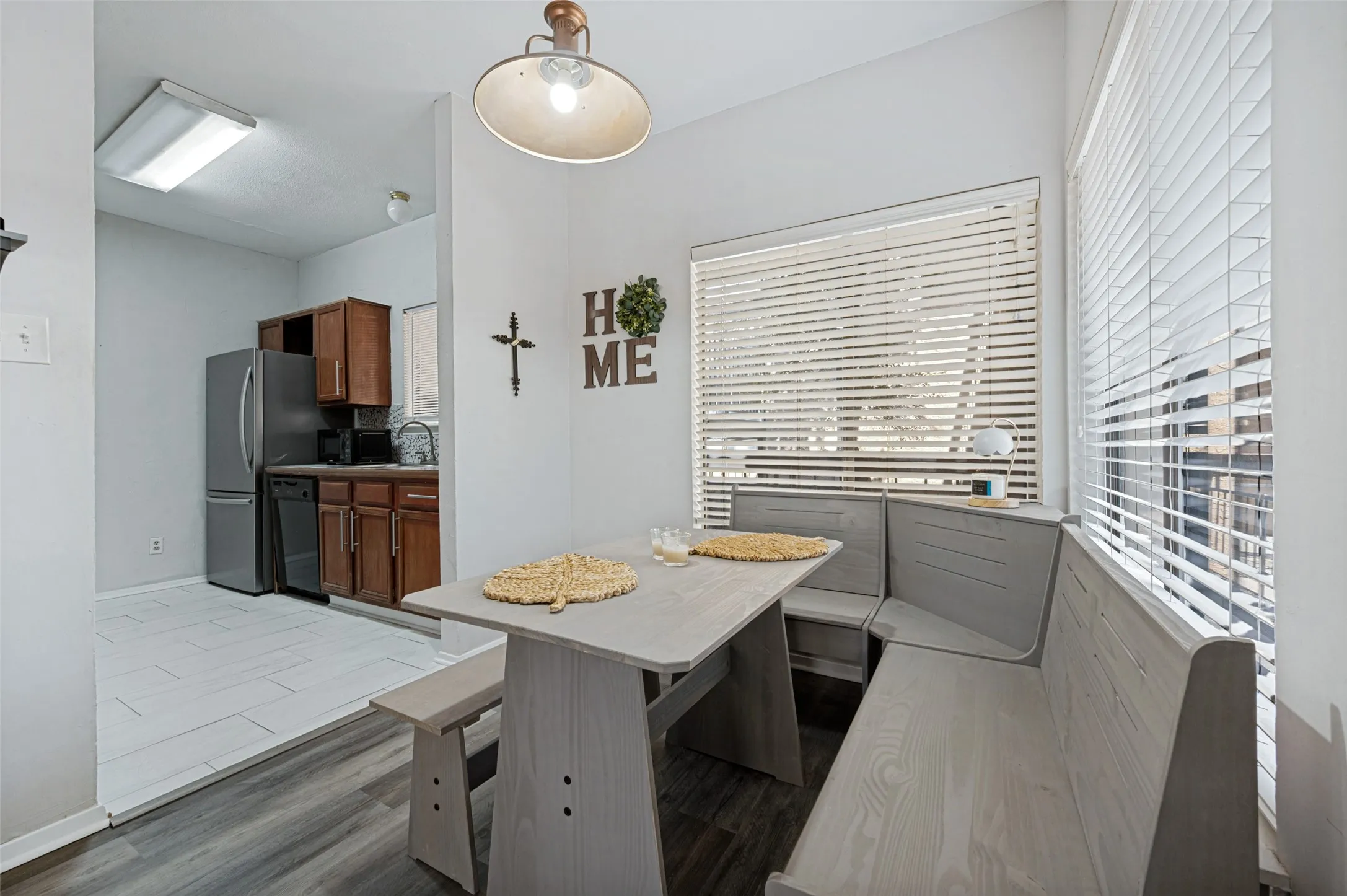 Built-in dining bench seating, wood-finish flooring, overhead lighting, and kitchen area with stainless steel refrigerator and dark wood cabinetry