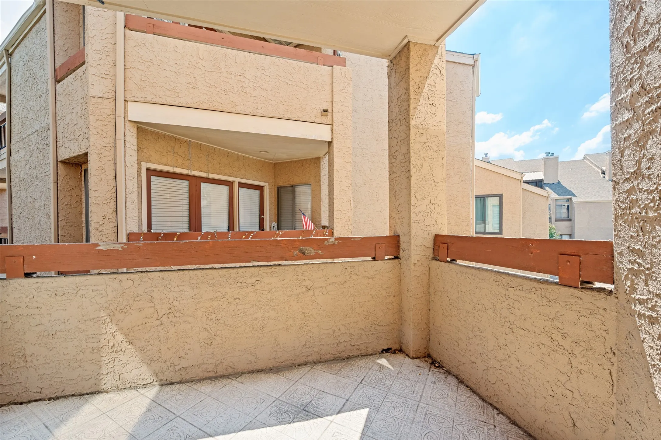 Exterior balcony featuring textured stucco walls, a wood-finished railing, and patterned tile flooring
