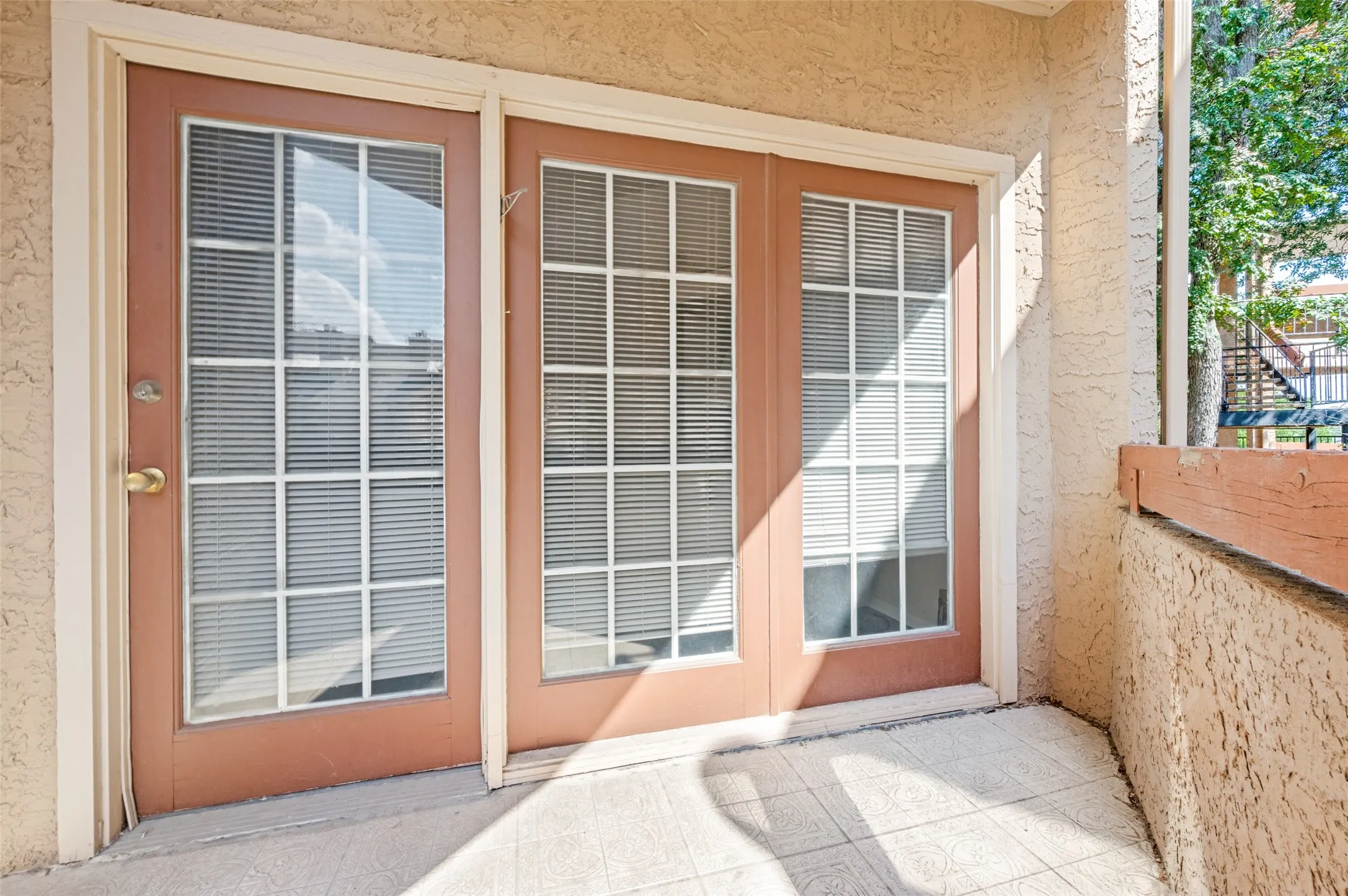 Back balcony double doors with grid-patterned glass, an exterior wall with stucco finish, and a tiled patio surface