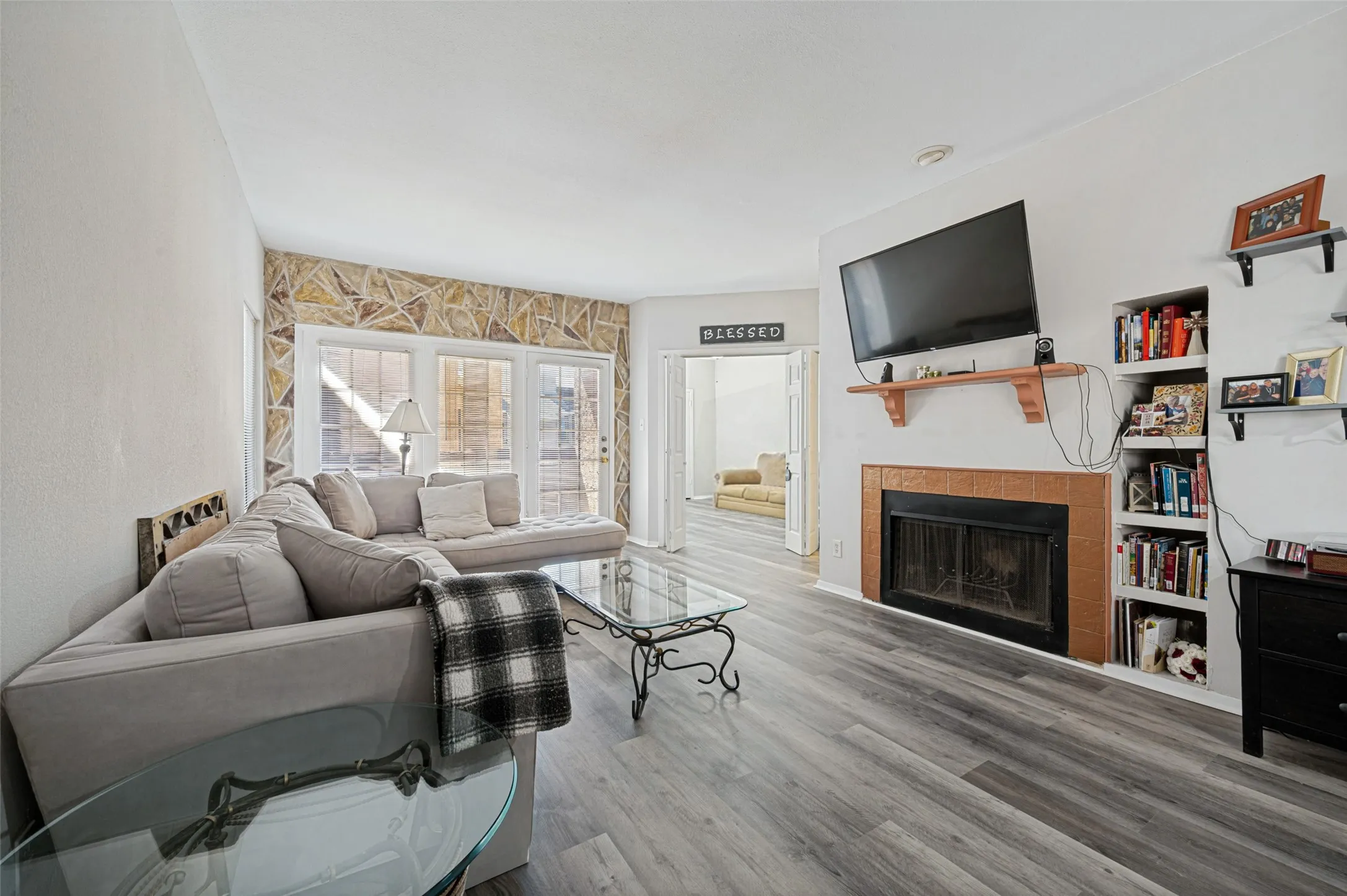 Wood-finish flooring, built-in shelving, stone accent wall, fireplace with tile surround, and direct outdoor access