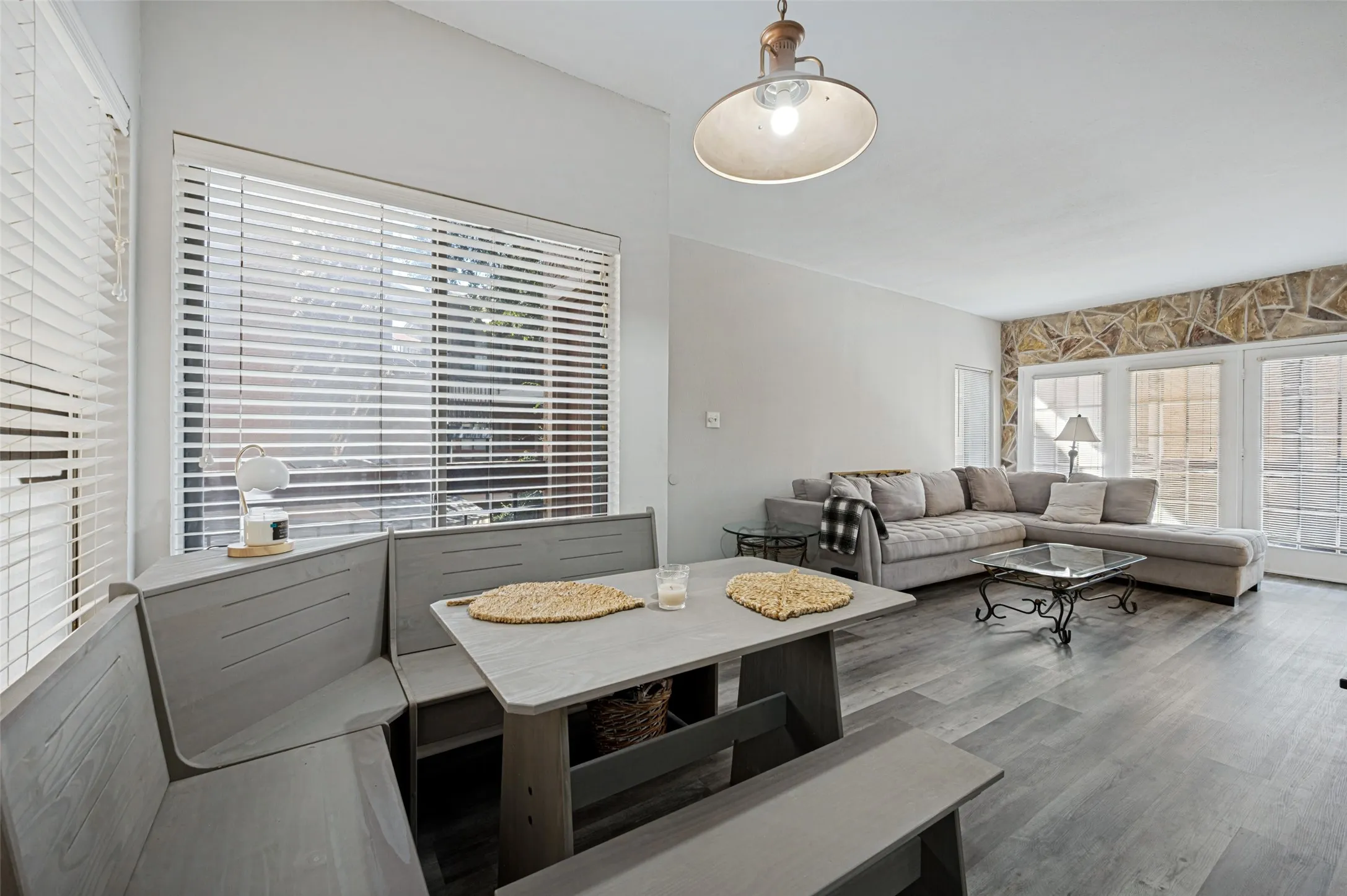 Wood-finish flooring throughout, vaulted ceiling, built-in banquette seating, stone accent wall, and multiple window panels