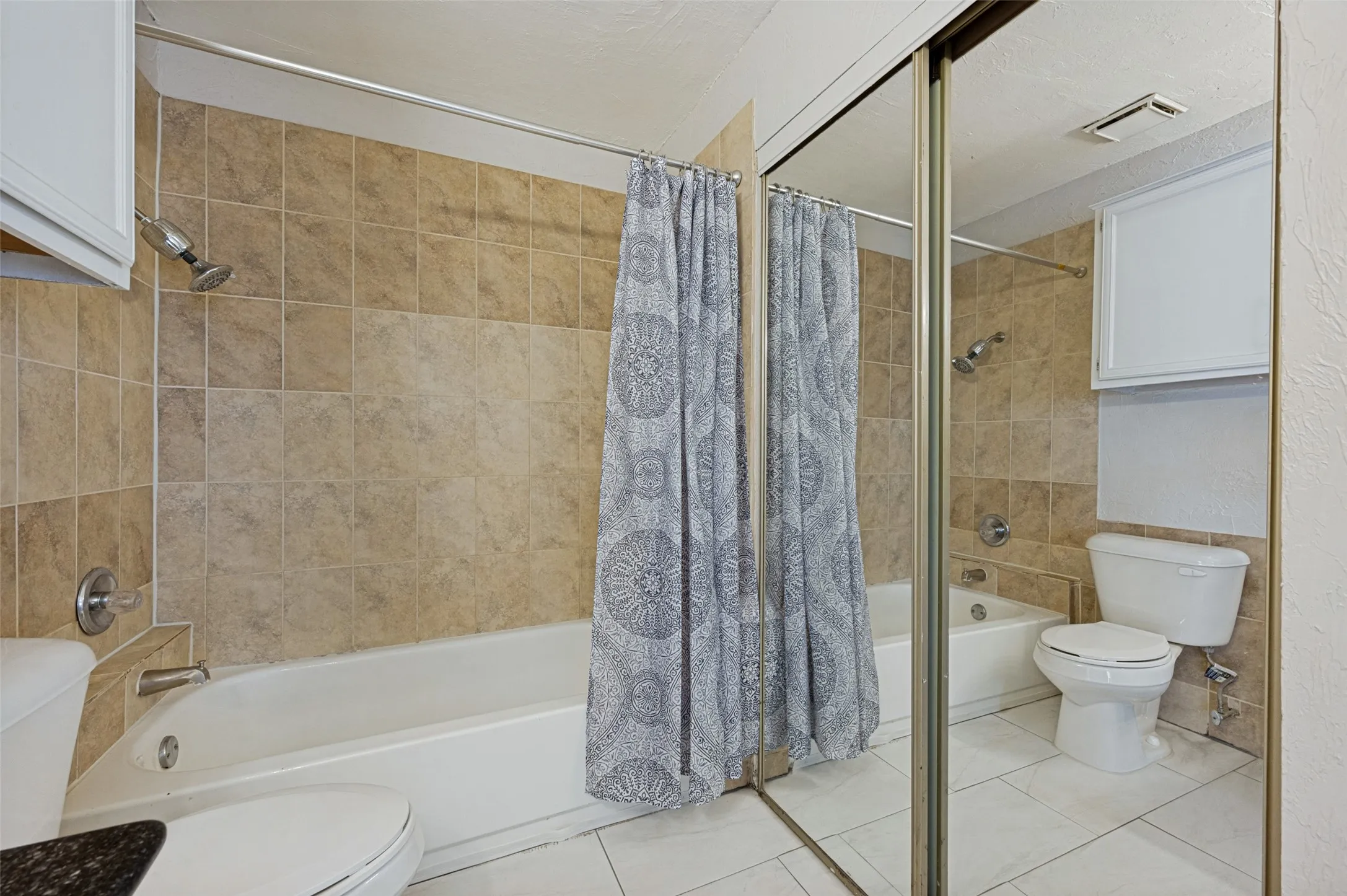 Full-sized bathtub with a shower fixture, tile surround, white vanity cabinetry, and mirrored closet doors