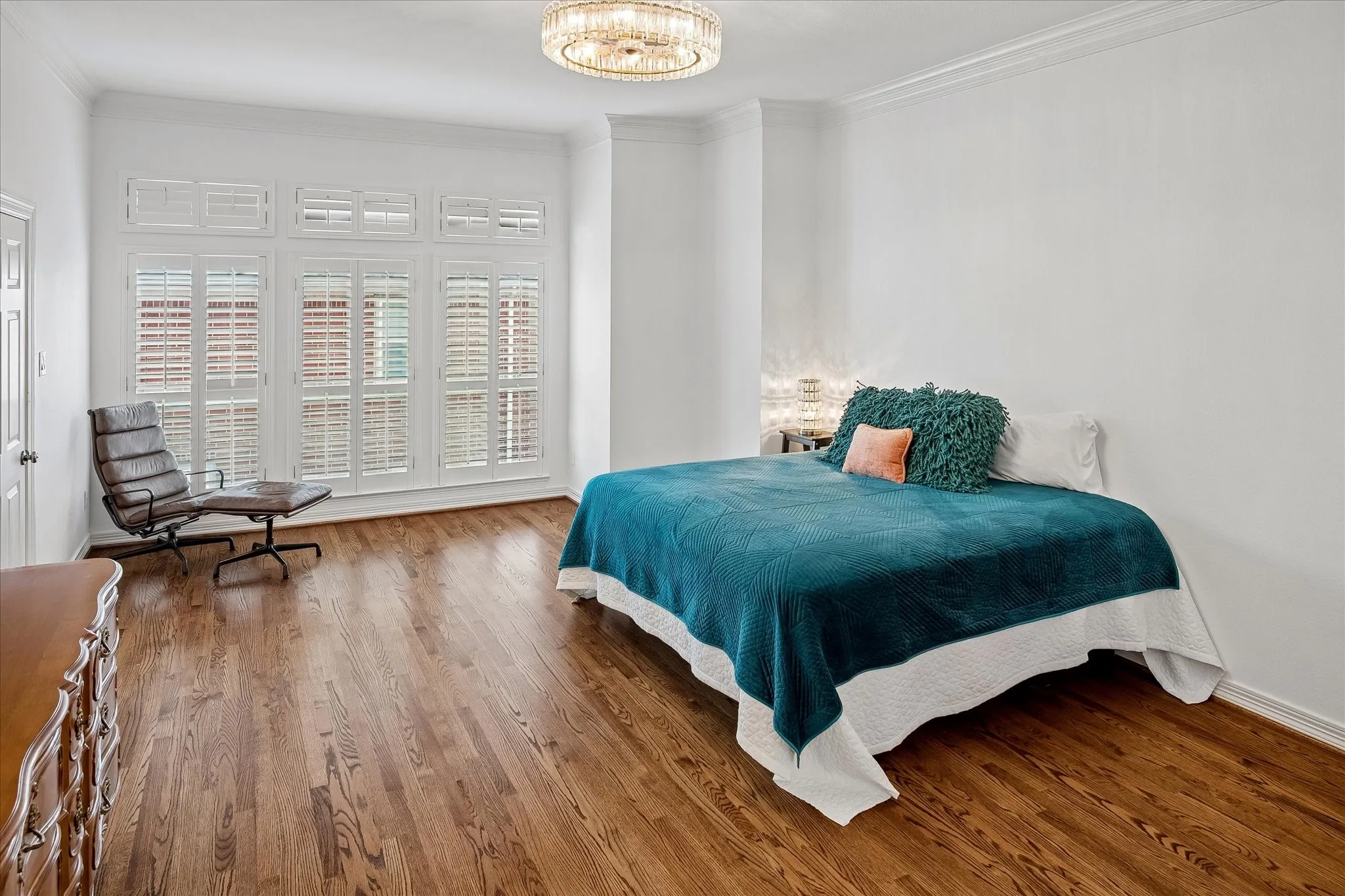 Hardwood flooring, crown molding, white walls, multiple windows with white plantation shutters, and a chandelier with a crystal-style shade