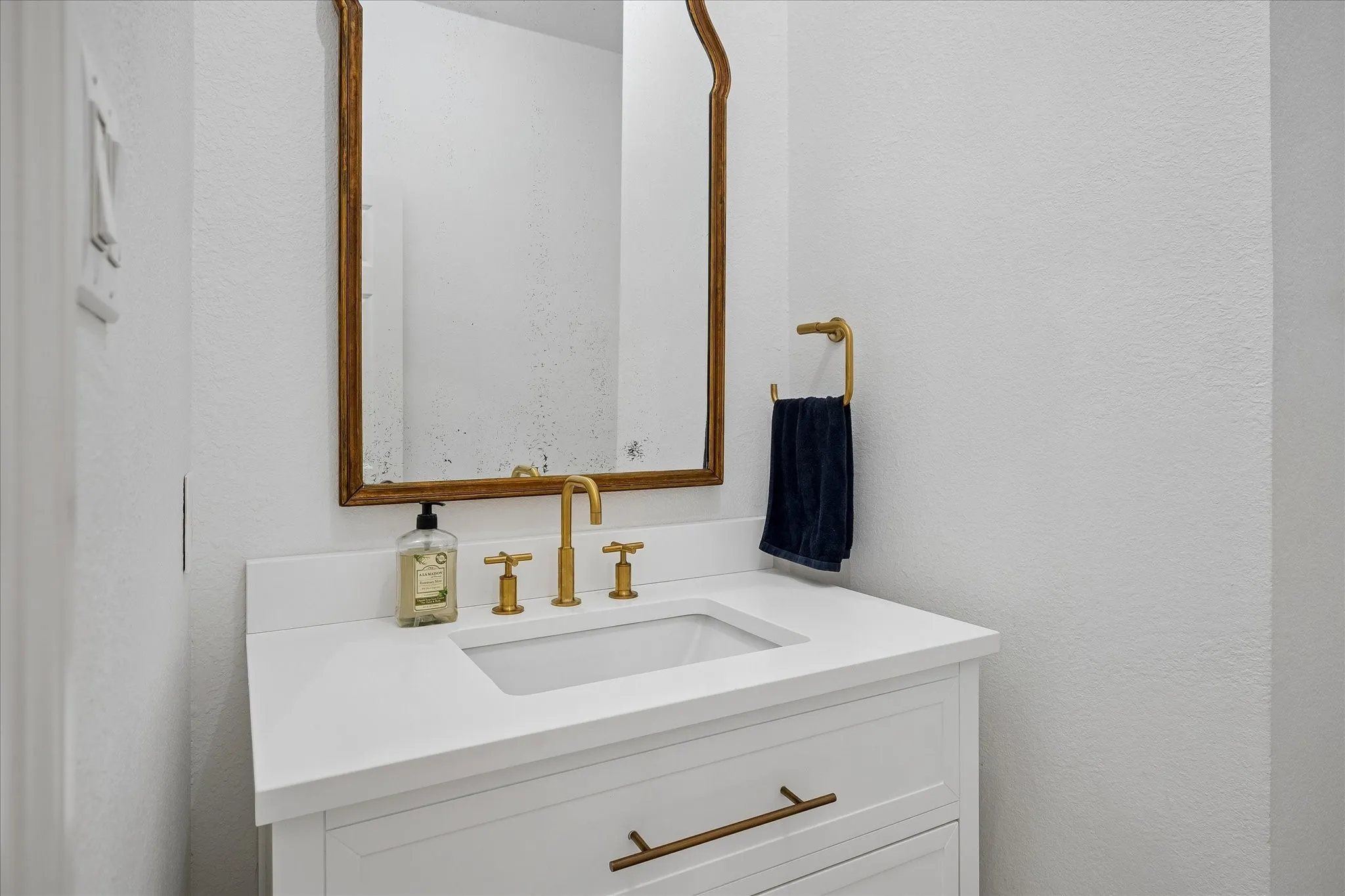 Elegant bathroom vanity featuring a white quartz countertop with an integrated rectangular sink, brass-finish three-hole faucet with lever handles, and soft-close cabinetry drawers