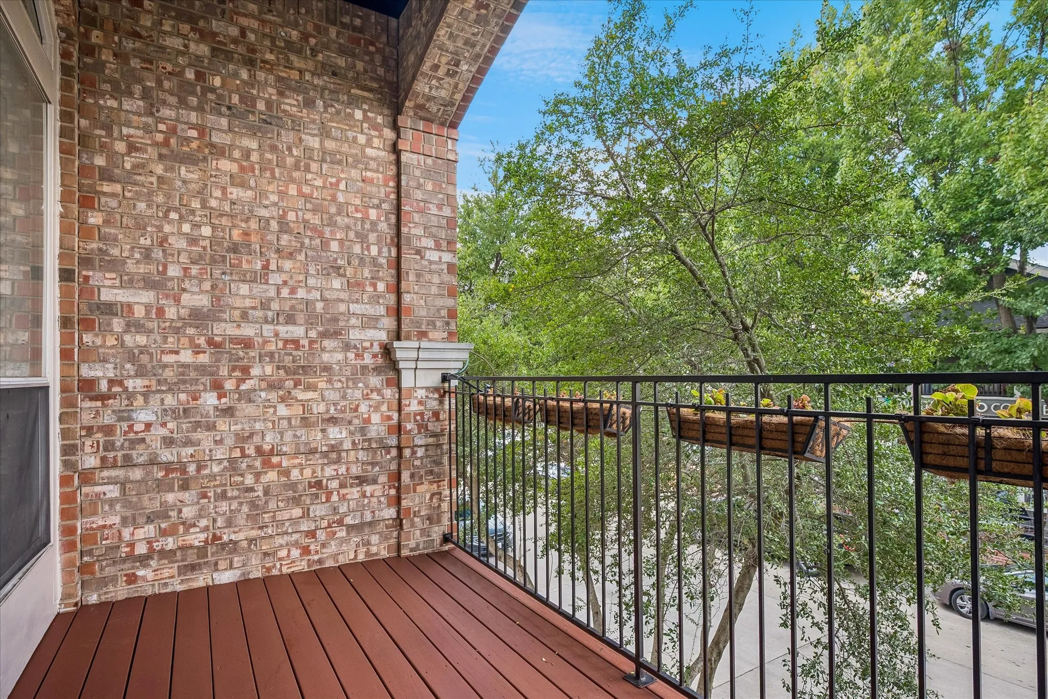 Elevated deck featuring rich wood-finish flooring and black metal railing, overlooking mature landscaping