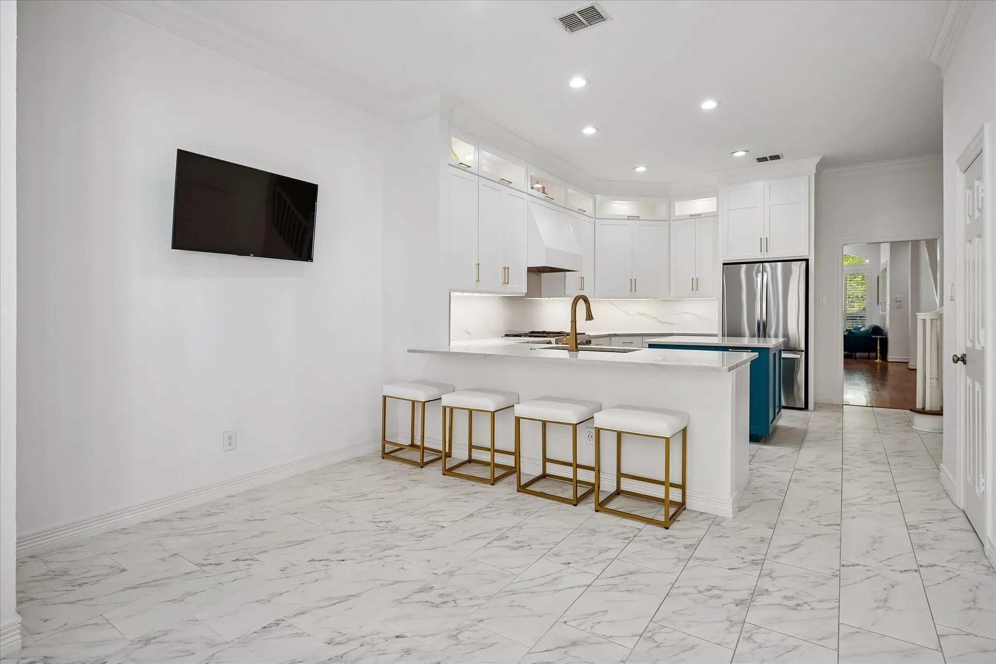 White marble-look floor tile, white shaker-style cabinetry, stainless steel refrigerator, white countertops, and a brass-finish faucet
