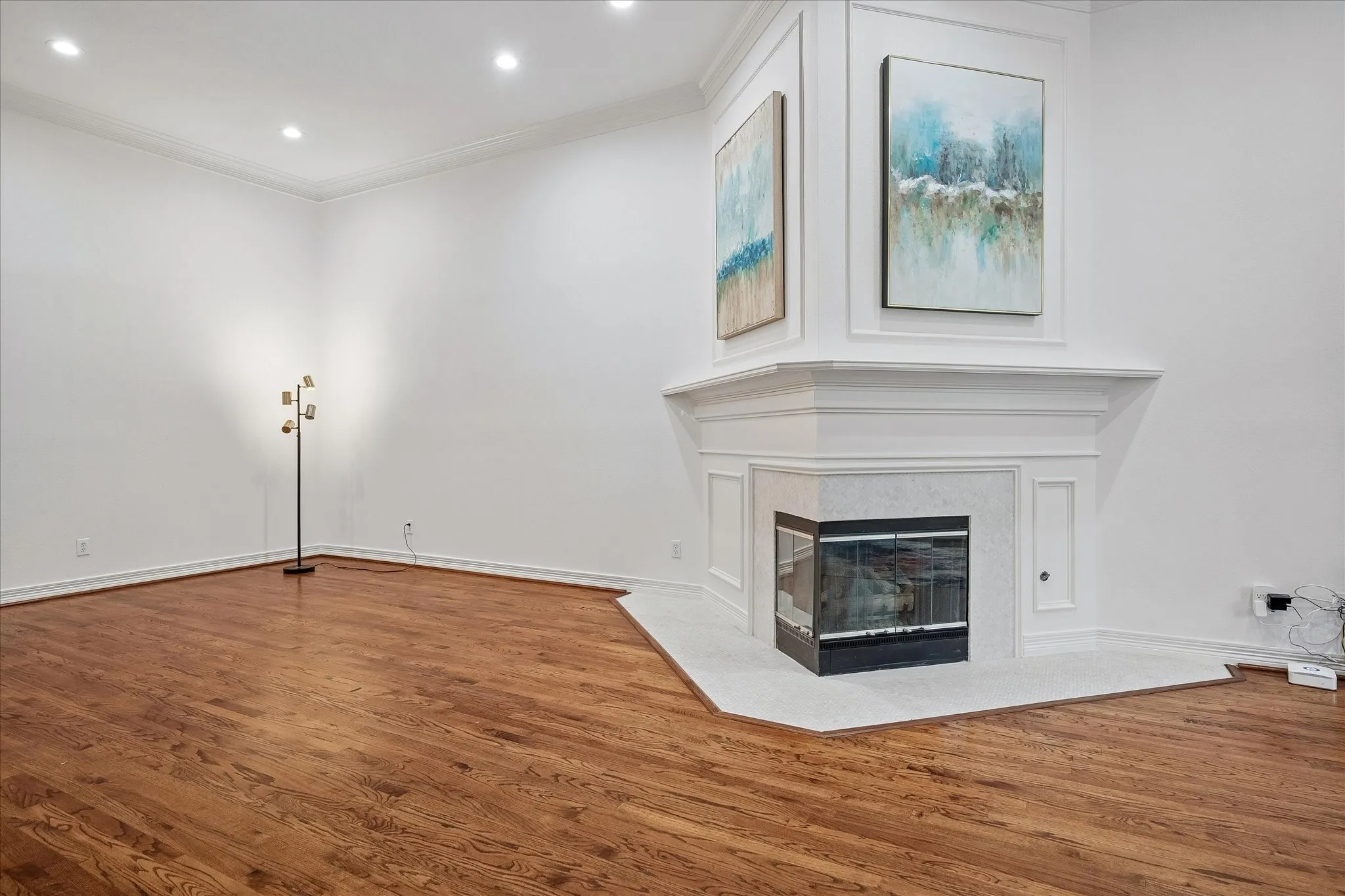 Hardwood flooring, recessed lighting, corner fireplace with a stone surround, and detailed crown molding