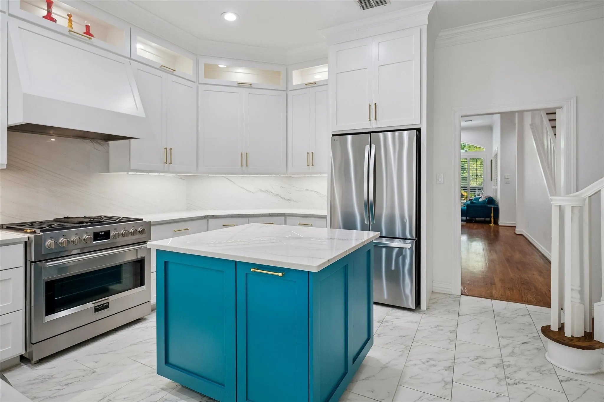 Bright kitchen featuring a vibrant blue island, white upper and lower cabinetry, stainless steel appliances, and white stone countertops