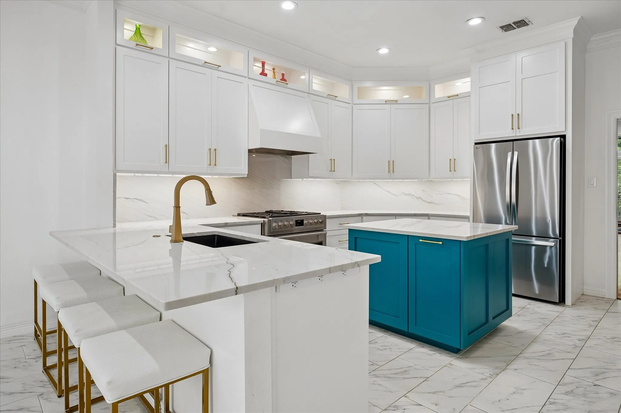 White cabinetry with brass hardware, quartz countertops, a teal-painted island, stainless steel appliances, and large format tile flooring