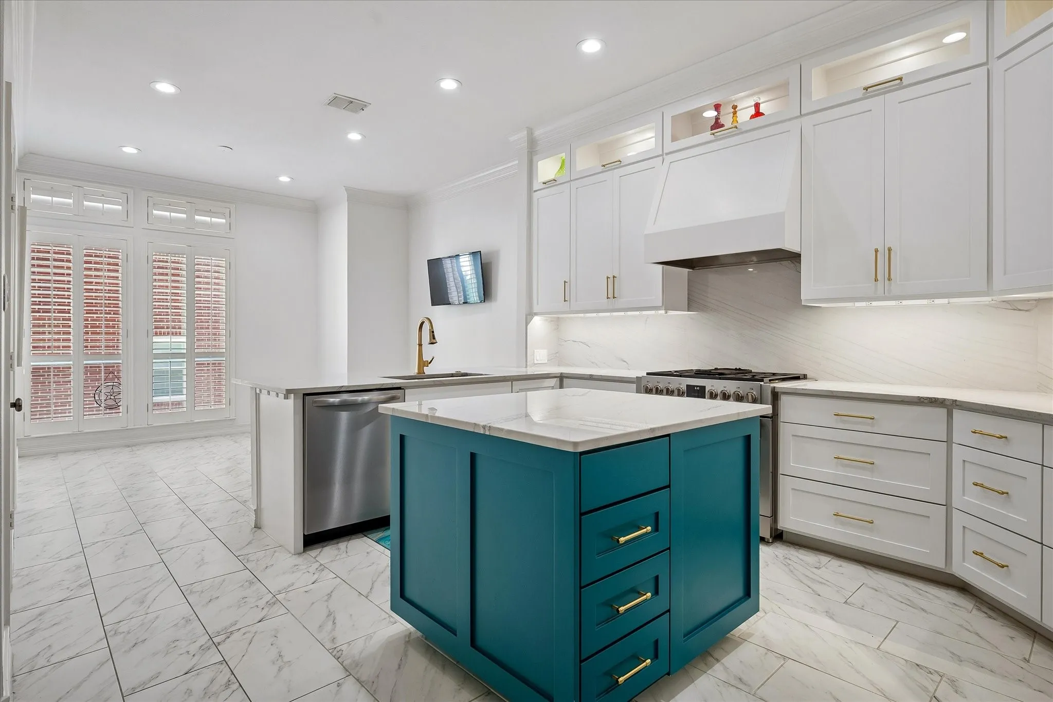 Sophisticated kitchen featuring soft-close cabinetry with brushed gold hardware, a striking teal-finished island with multiple drawers, quartz countertops, stainless steel appliances including a gas cooktop, and tile flooring throughout