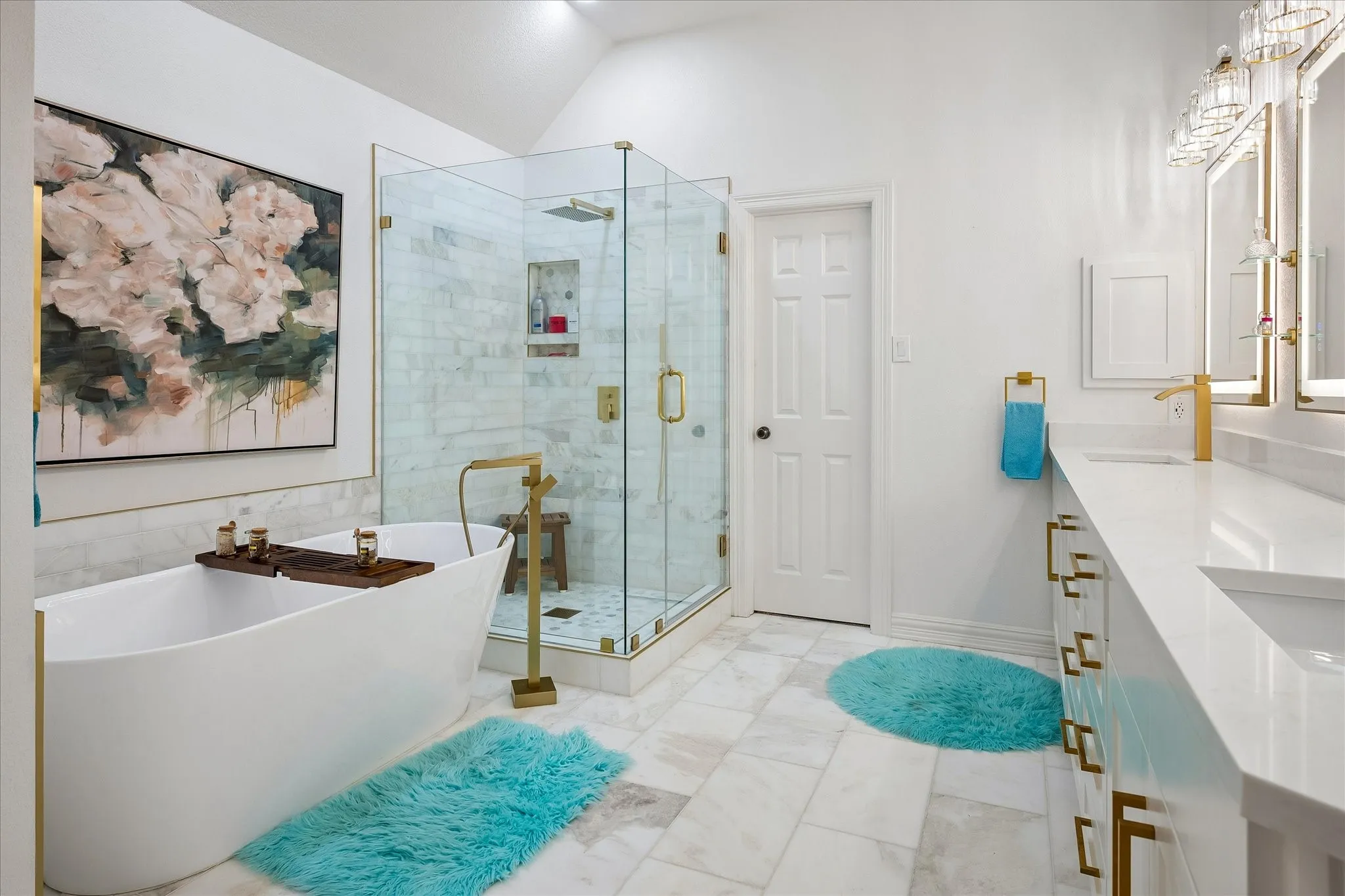 Spa-inspired primary bathroom featuring a freestanding soaking tub, walk-in shower with glass enclosure and brass fixtures, dual vanities with white countertops, polished tile flooring, and framed floral artwork