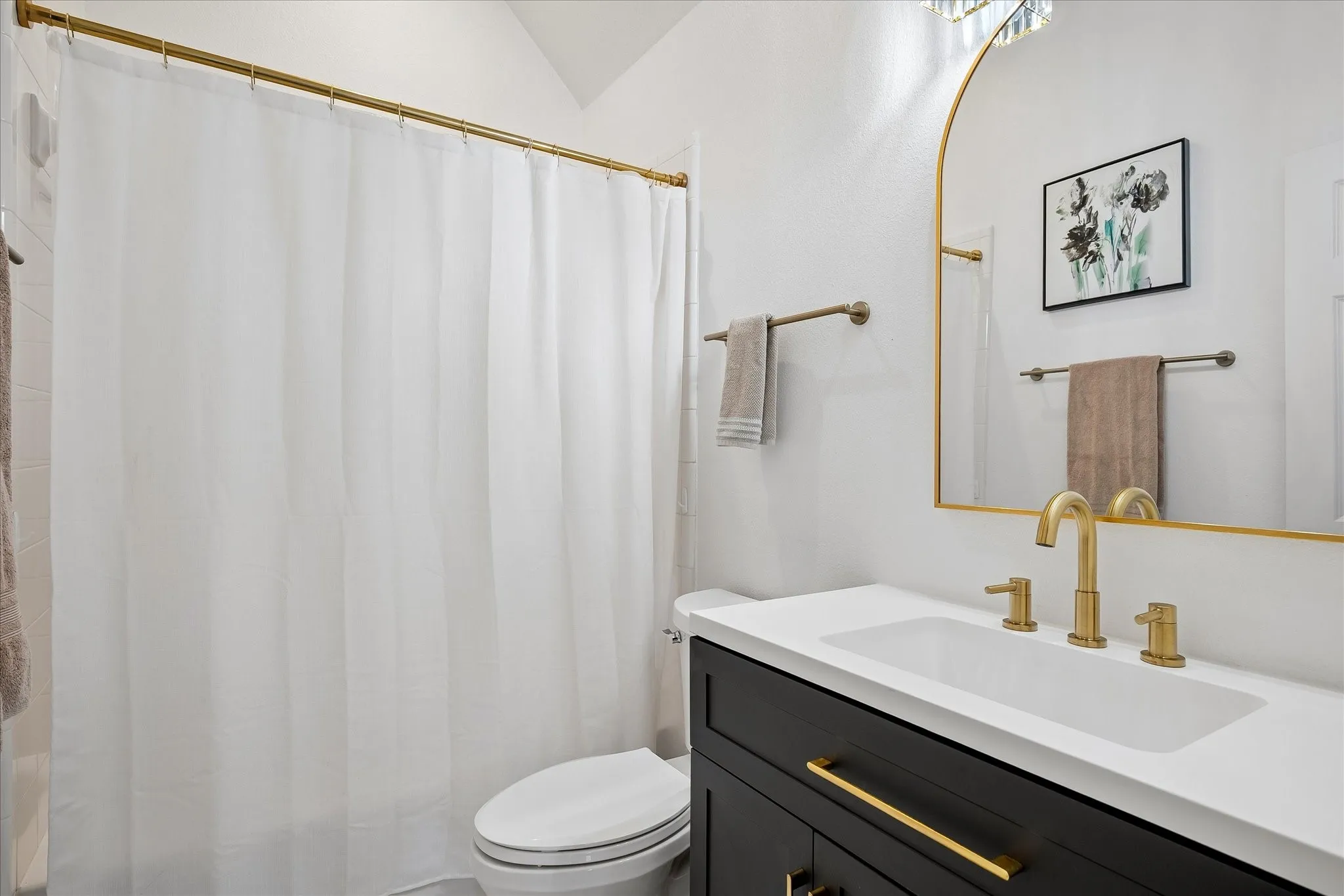 Vanity with a white countertop and integrated sink, gold-finish faucet, and dark wood-finish cabinetry with gold-finish hardware